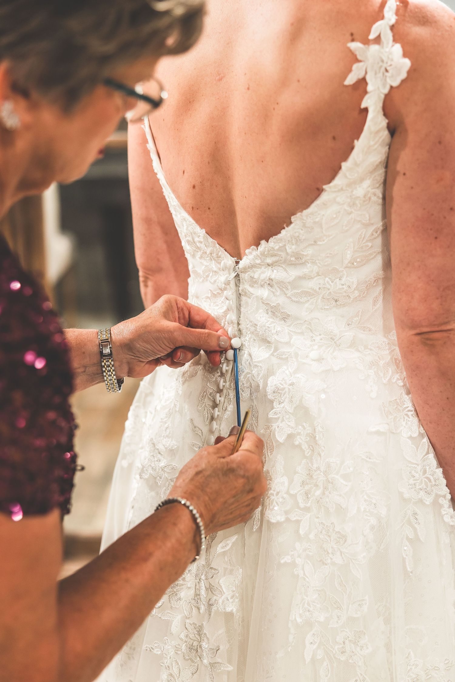 Close-up of wedding dress being buttoned up during final preparation moments.