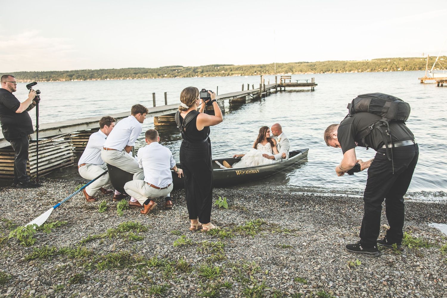 Wedding party celebrating on a rocky shoreline at sunset.