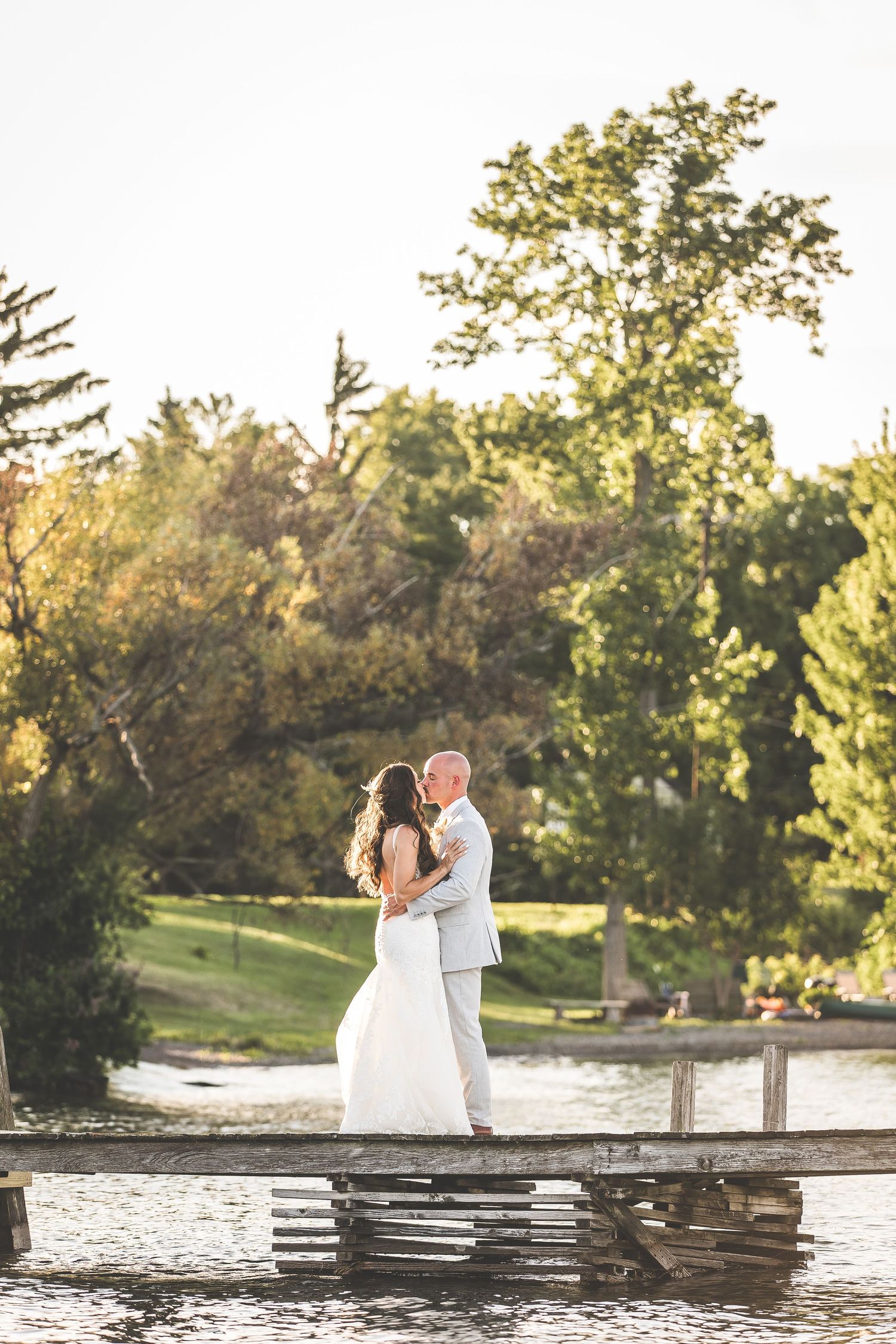 Wedding couple shares intimate moments on wooden pier during golden hour by the water.