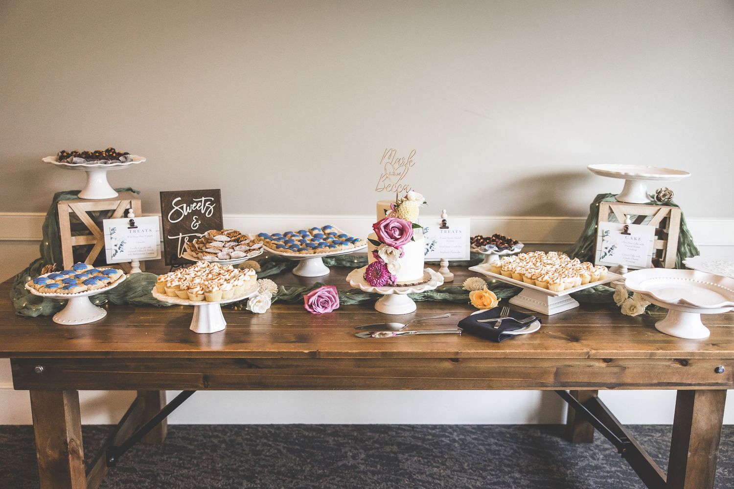 Long rustic wooden table displaying an assortment of wedding desserts and cakes.