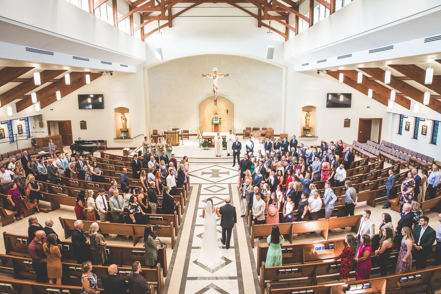Interior view of a modern church sanctuary with wooden beams and pews filled with wedding guests.