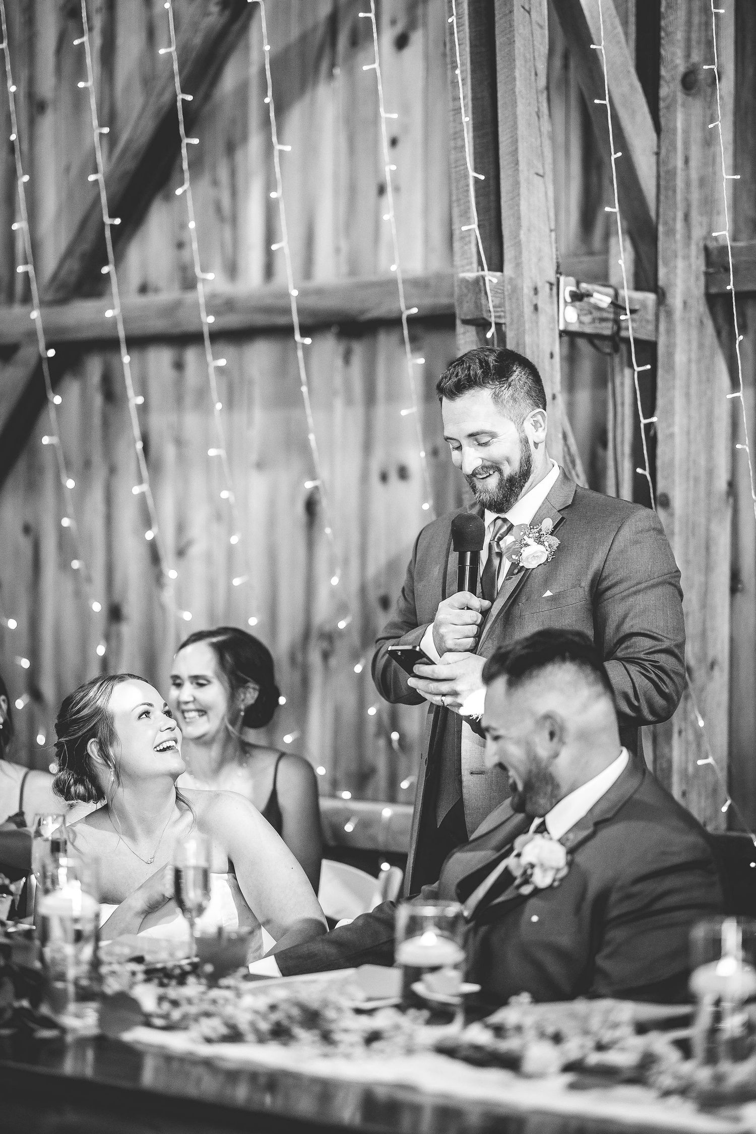 Black and white photo of wedding party seated at head table during reception speeches.