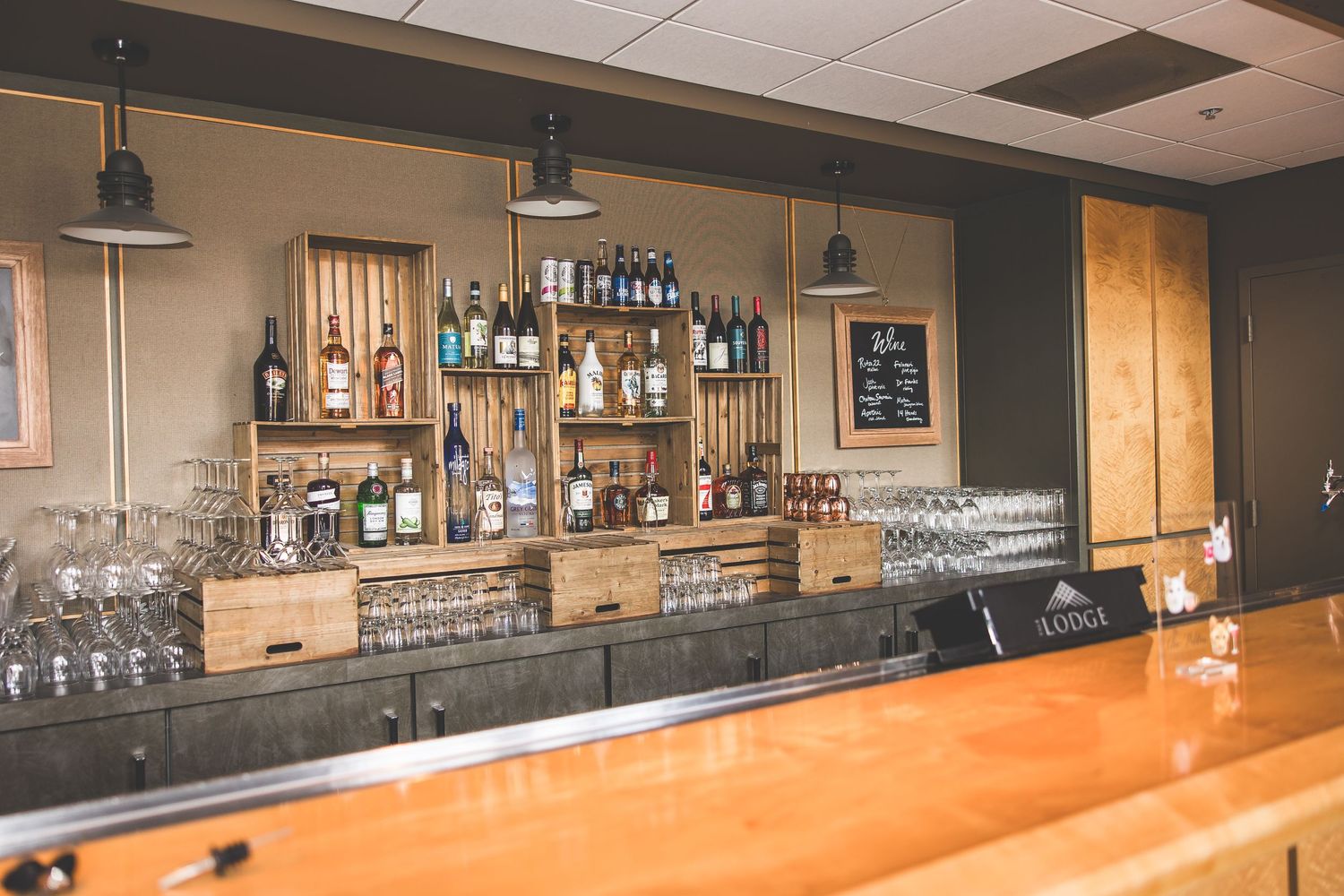 Modern bar setup with wooden counter and illuminated bottle display shelving.