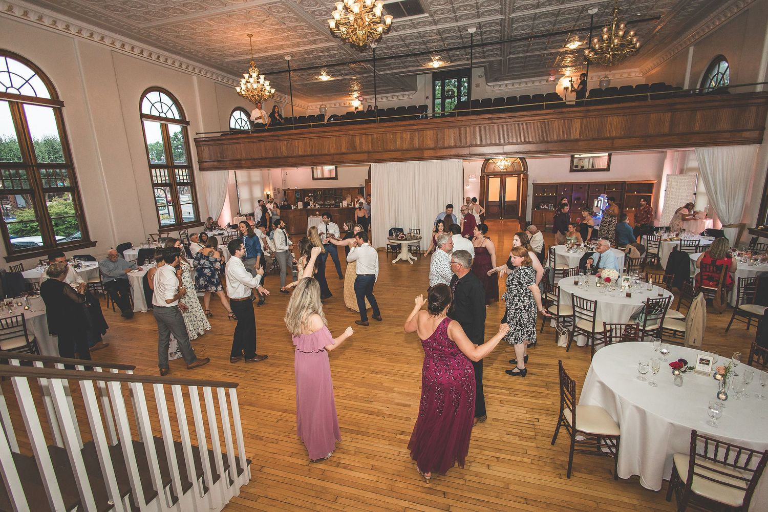 Wide view of a wedding reception venue with guests dancing and dining at round tables.