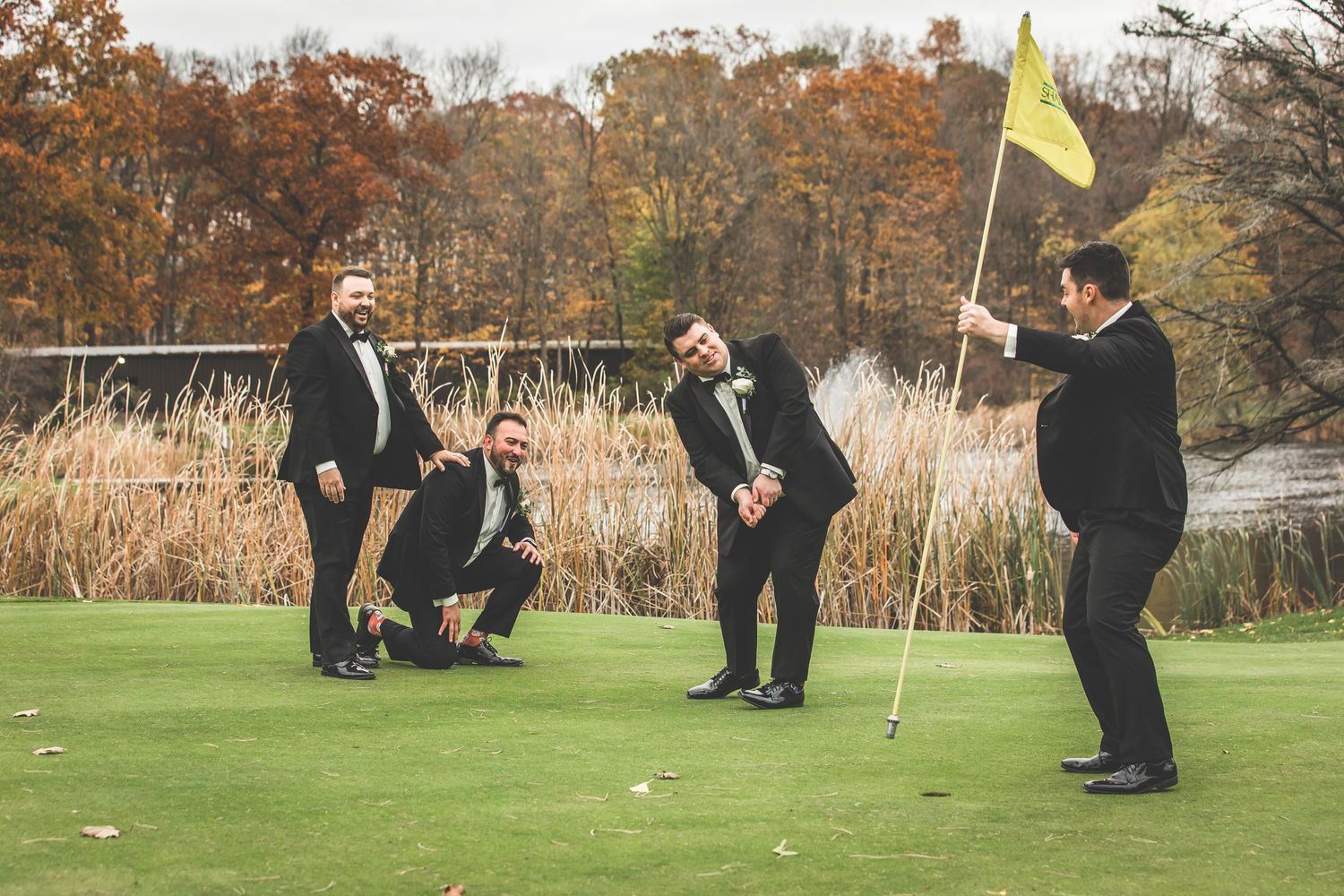 Groomsmen playing golf on course during wedding celebration with autumn scenery.