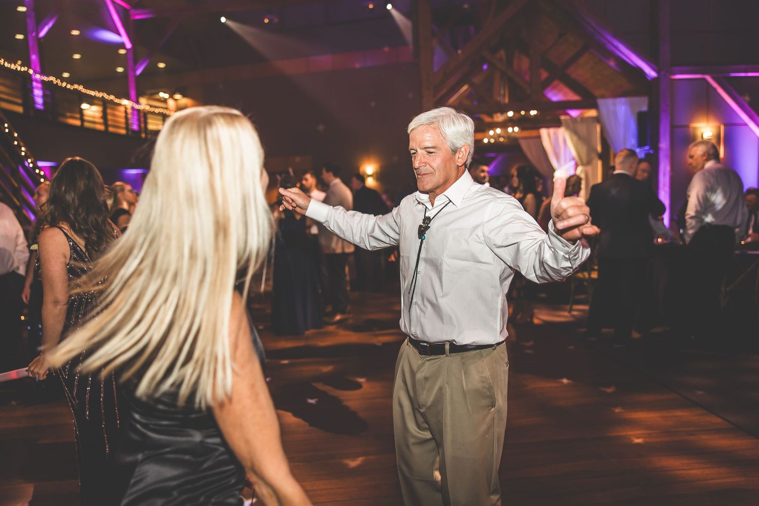 Dance floor filled with wedding guests celebrating under purple ambient lighting.