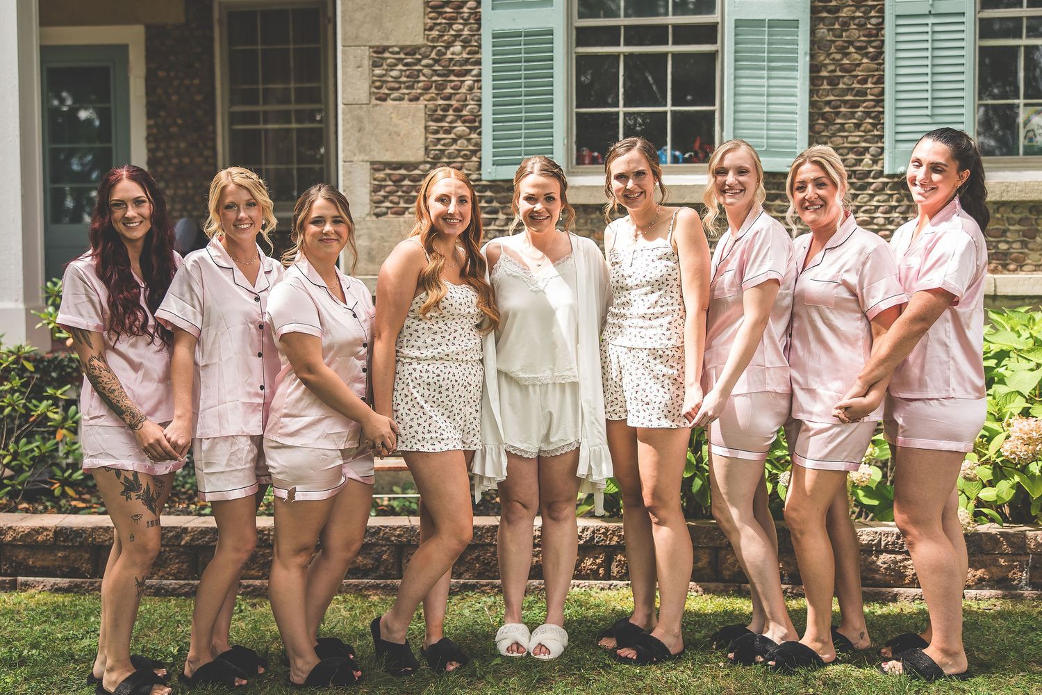 Group wearing matching pink and white loungewear poses together on front porch steps.