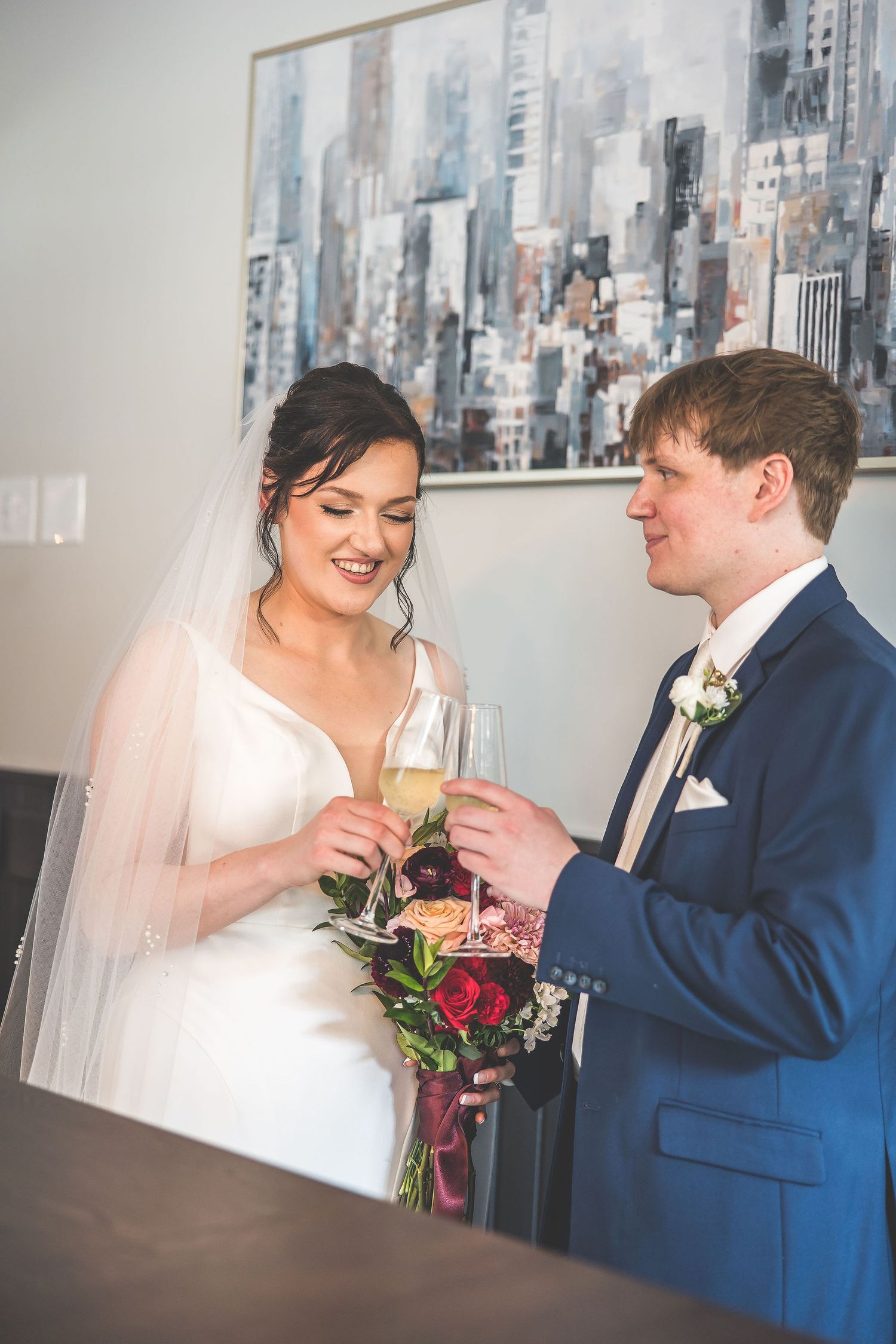 Wedding celebration with champagne toast against city skyline artwork backdrop.