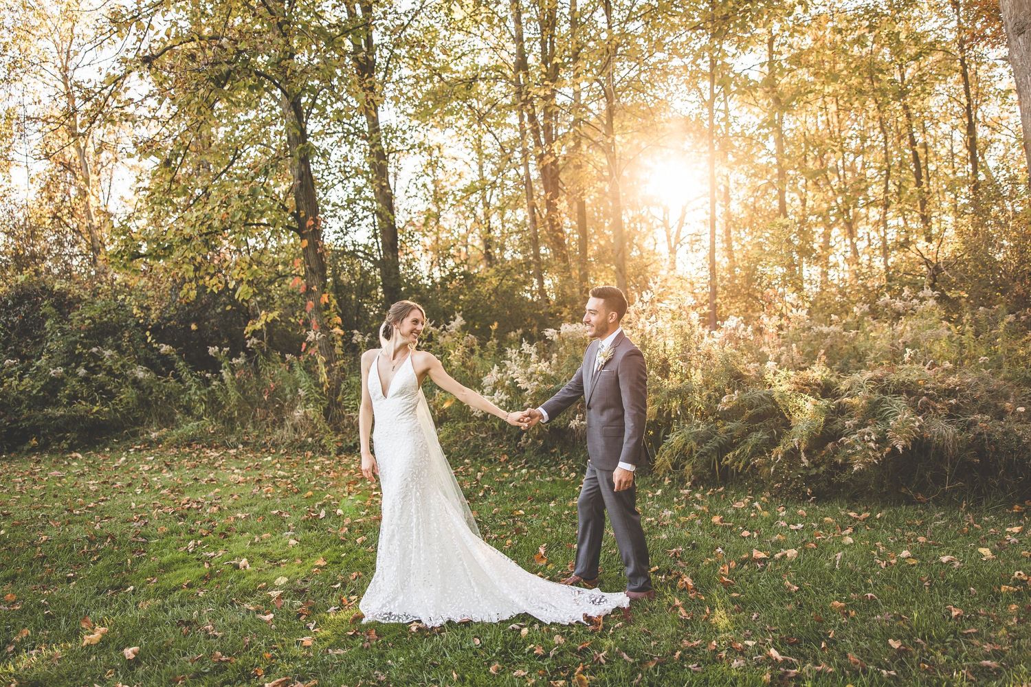Wedding couple dancing in golden sunlit forest clearing with bride's dress trailing behind.