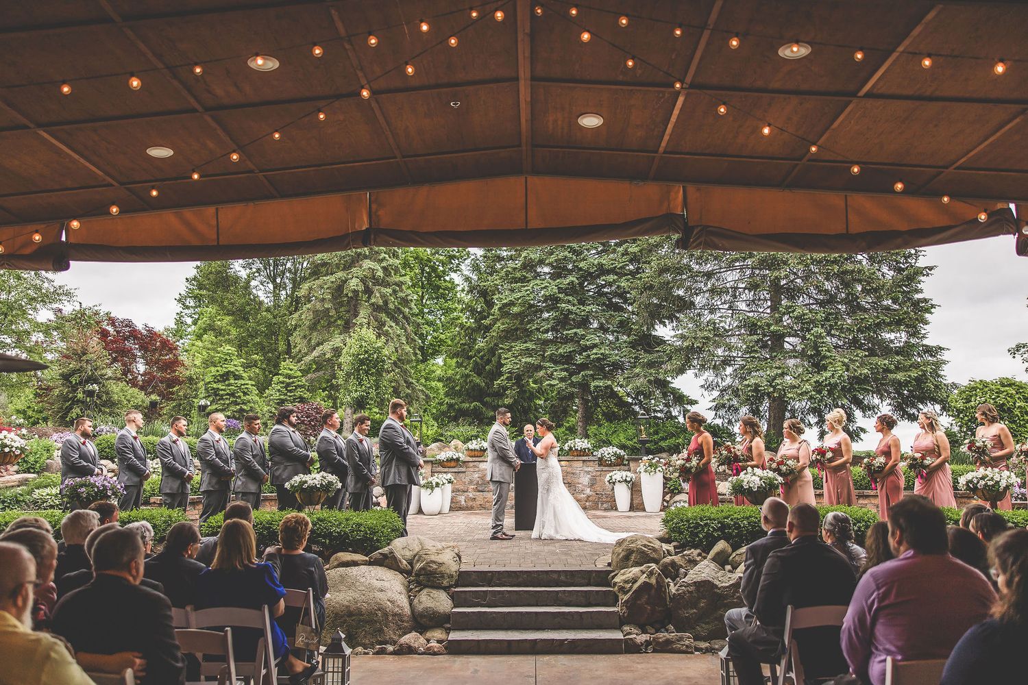 Wedding reception venue with string lights and guests seated under covered outdoor pavilion.