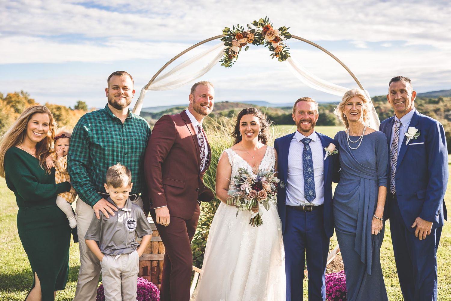 Extended family and wedding party members pose together for group photos on grassy hillside.