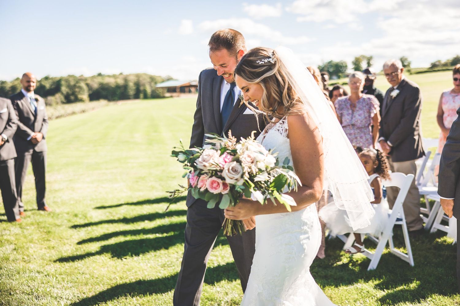 An outdoor wedding celebration with beautiful floral bouquets on a grassy hillside.