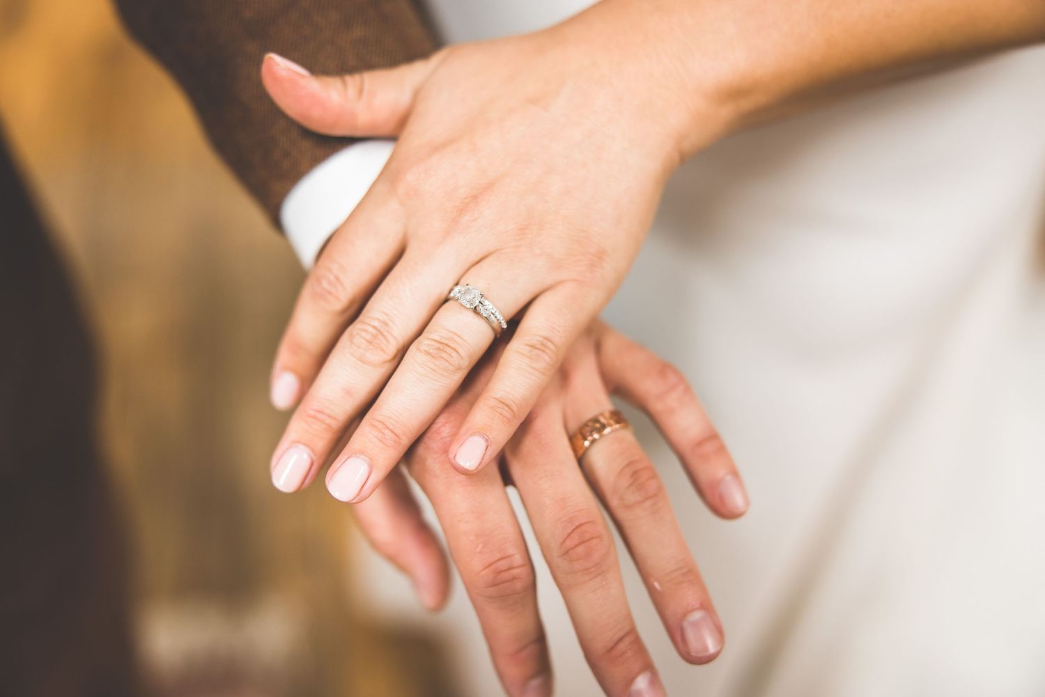 Close-up of hands showing wedding rings against white dress fabric.