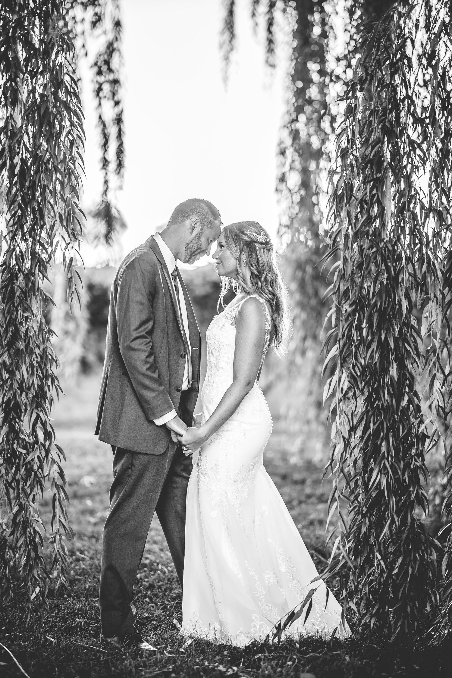 Artistic black and white wedding photo with dramatic willow tree framing.