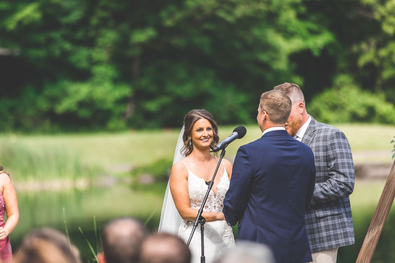 Wedding ceremony in progress under wooden arch with natural greenery backdrop.