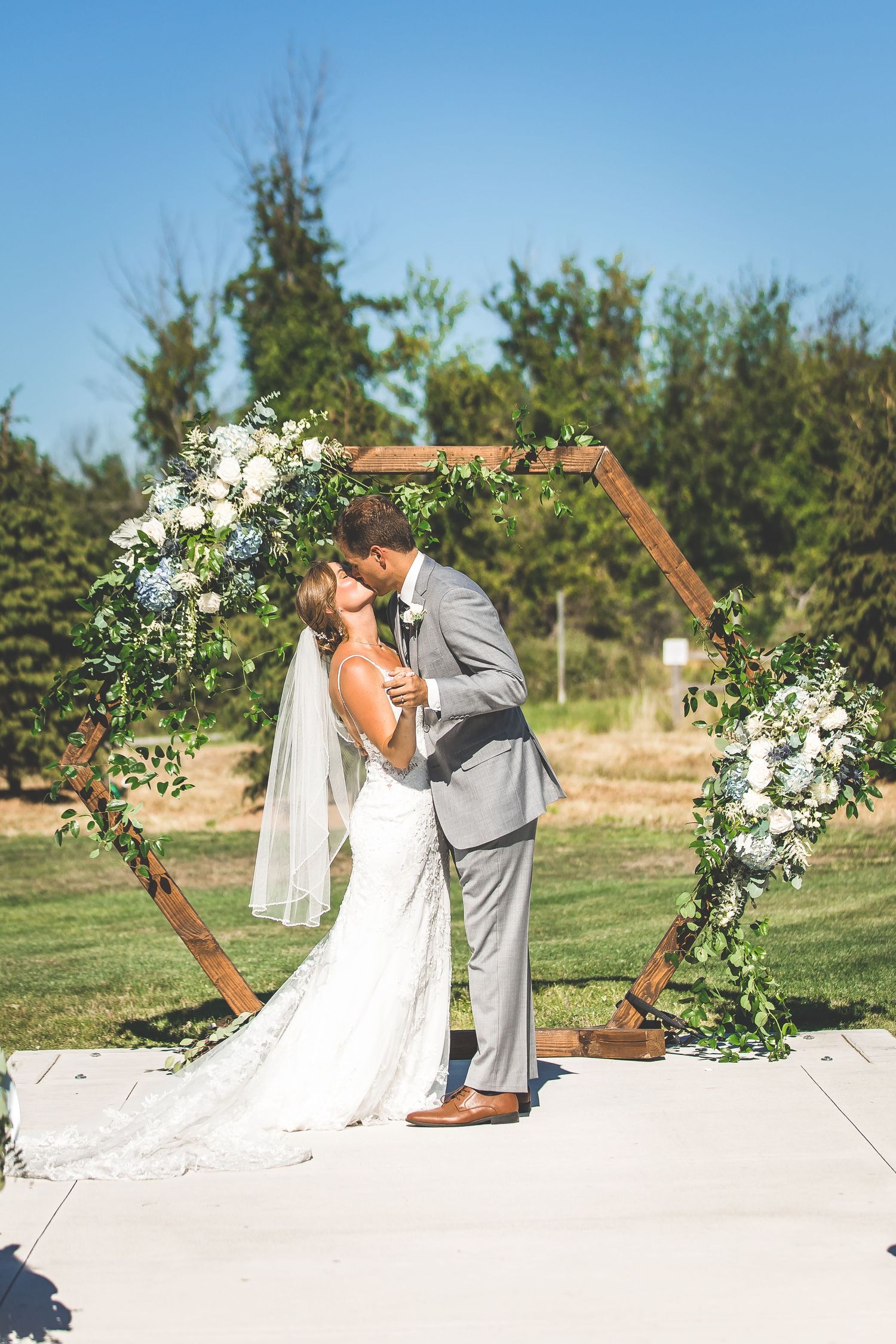 Wedding ceremony site with wooden hexagonal arch decorated with white flowers and greenery.