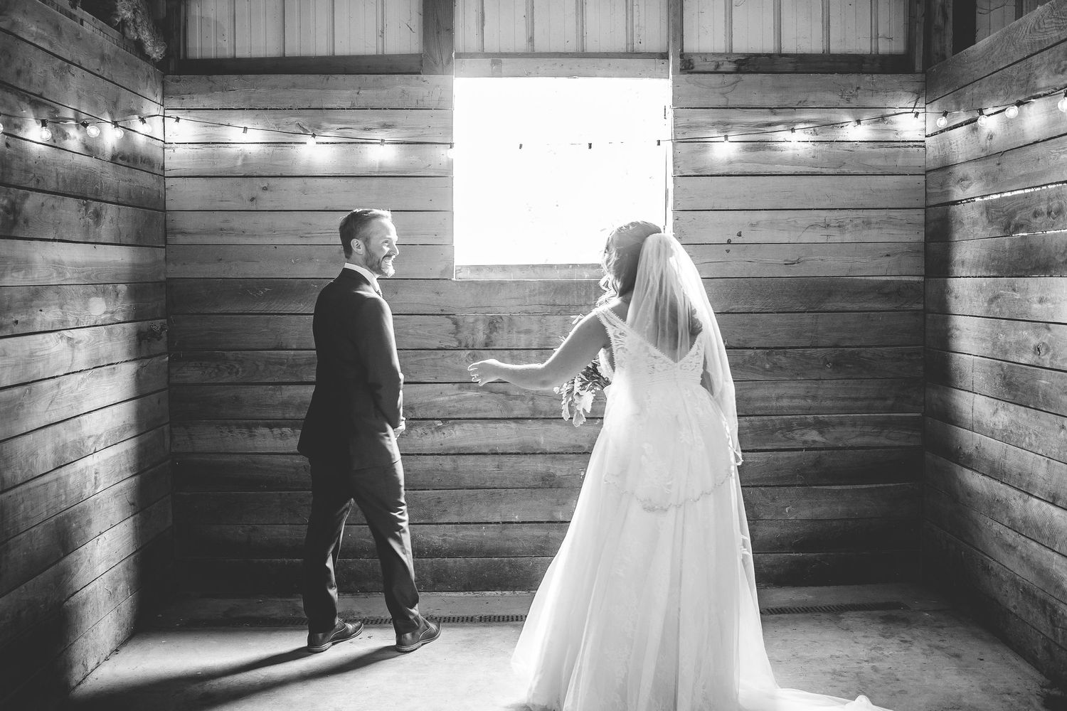 Black and white photo of a rustic barn interior with wooden walls and string lights.