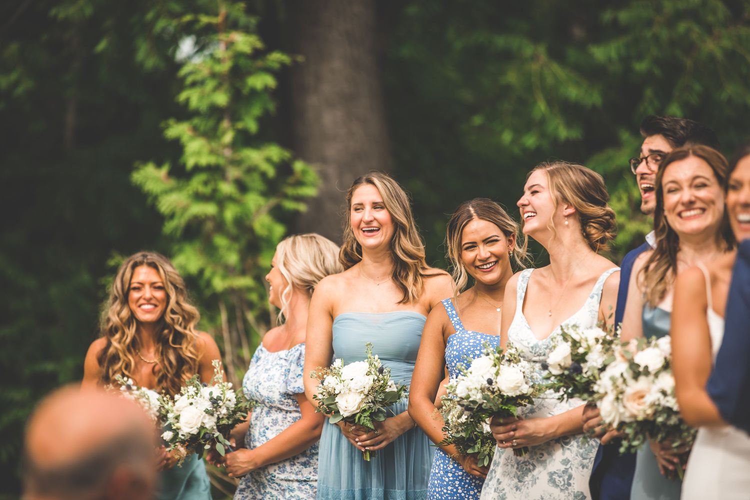 Wedding party members in blue dresses holding white floral bouquets during outdoor celebration.