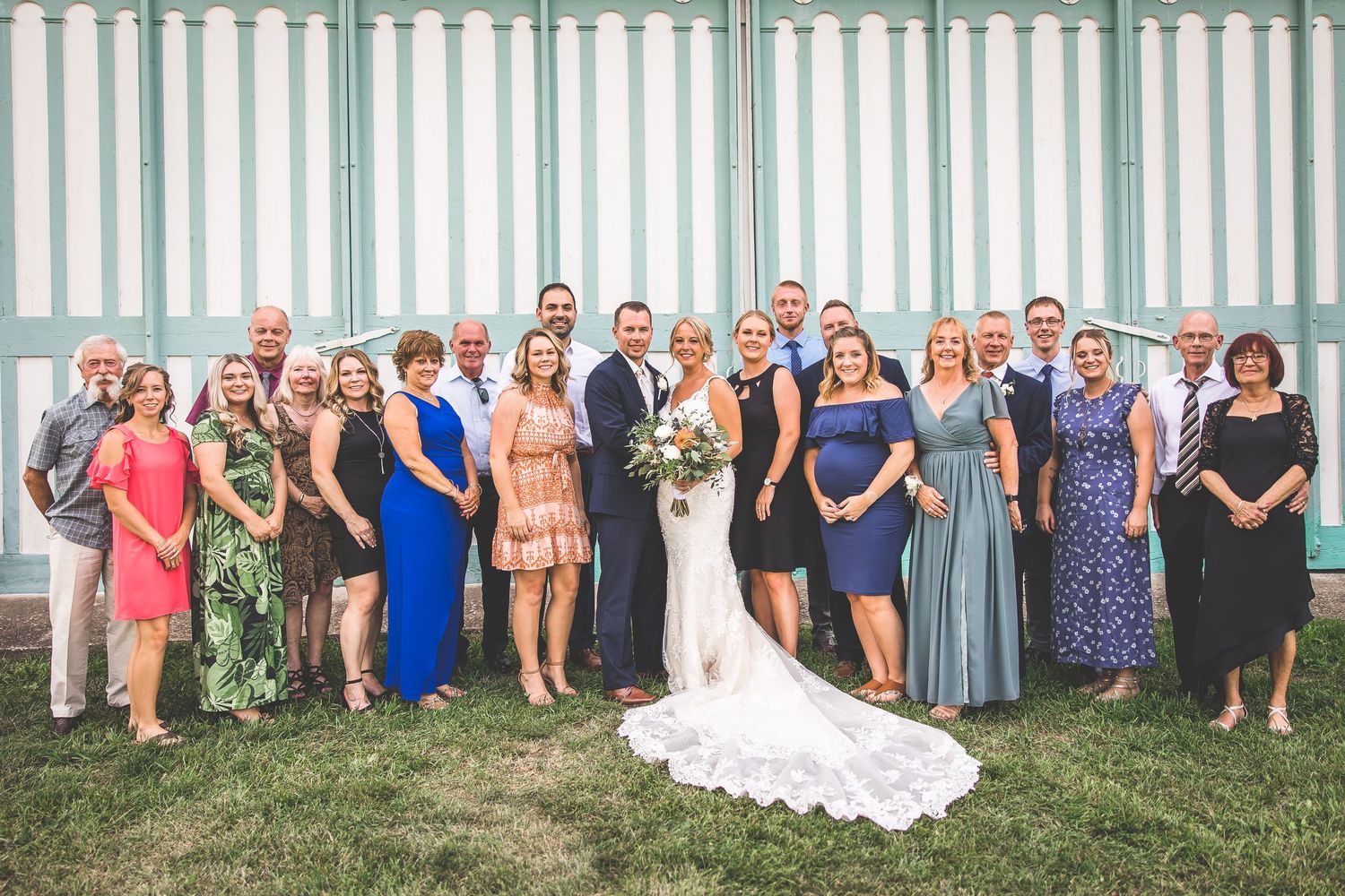 Large group wedding photo with rustic white fence backdrop.