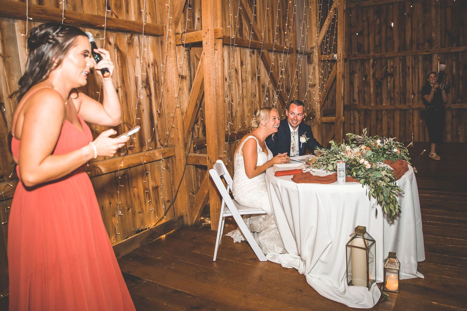Wedding reception guests enjoying dances in a rustic barn decorated with string lights.