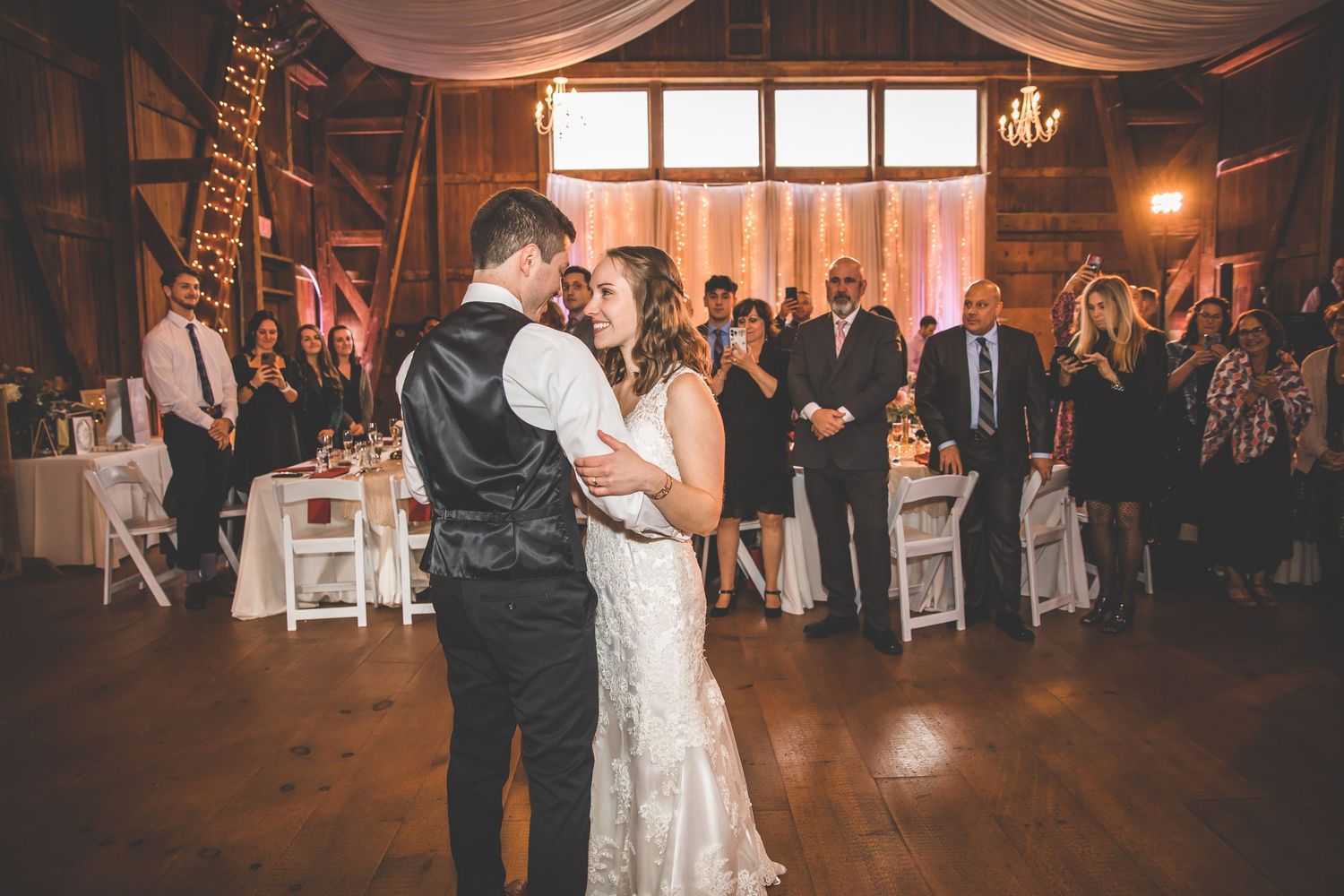 Wedding reception dance in a rustic barn venue with romantic lighting and fabric draping.