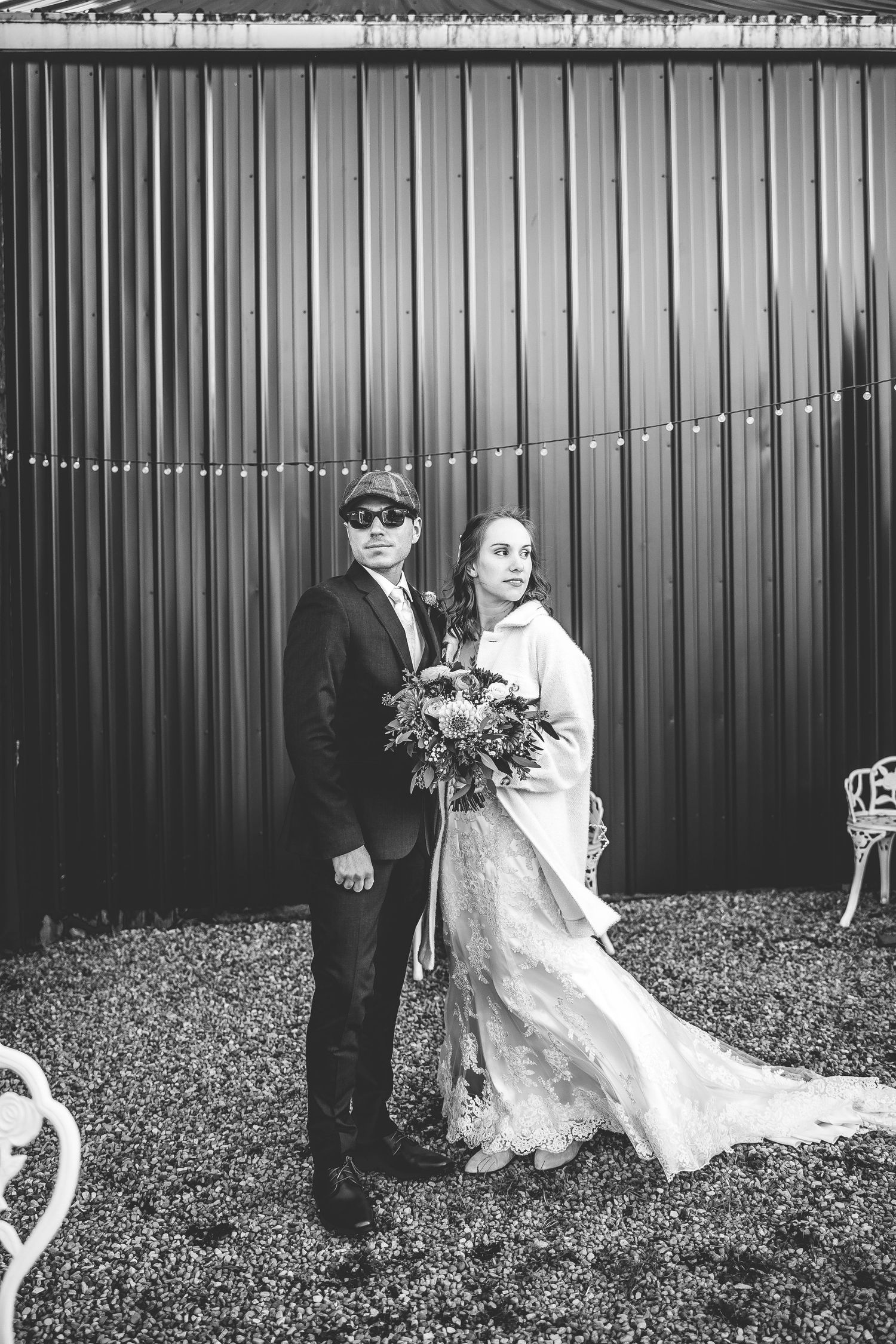 Black and white wedding portrait against metal wall with string lights.