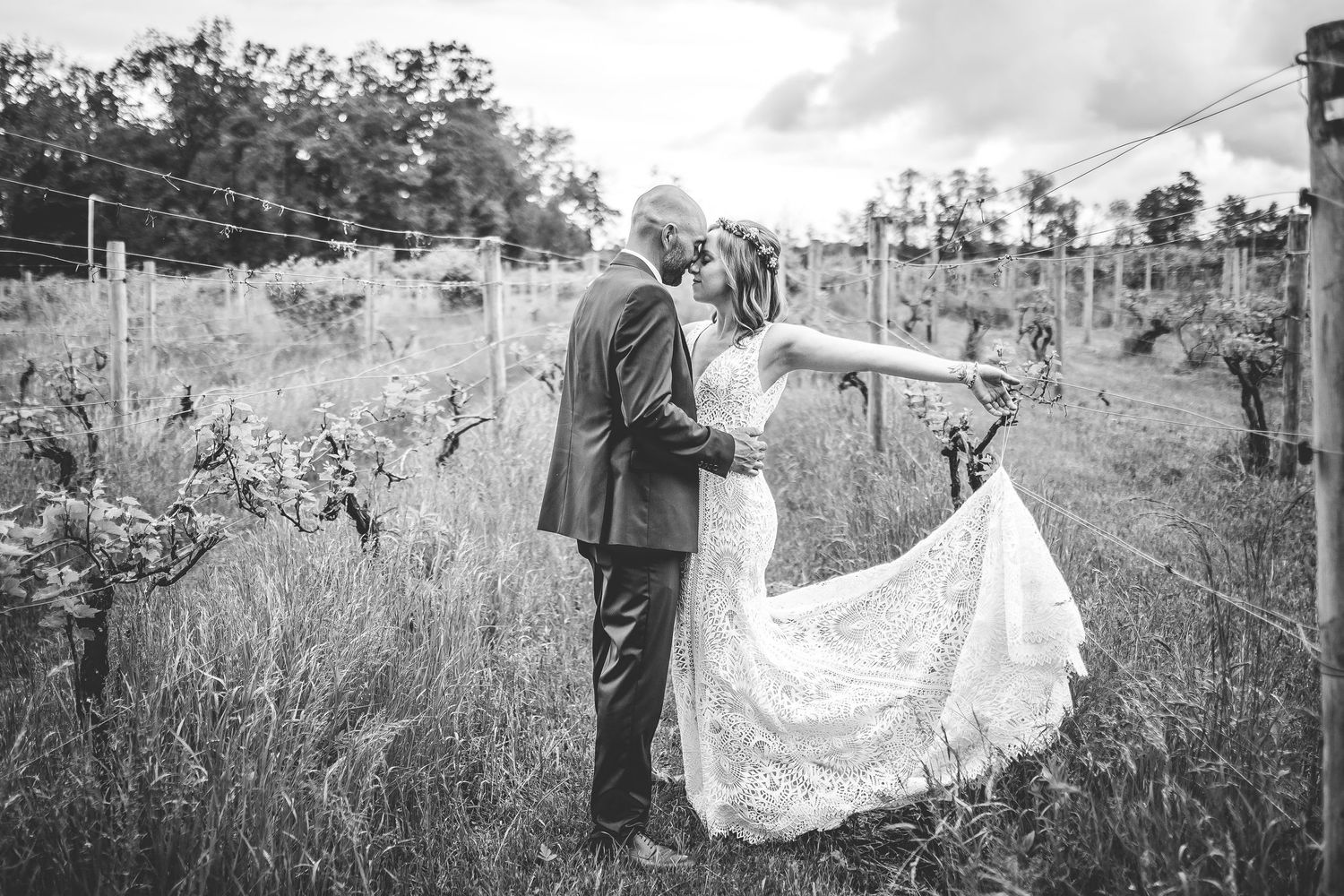 A black and white photo showcasing an elegant lace wedding dress train in a countryside setting.