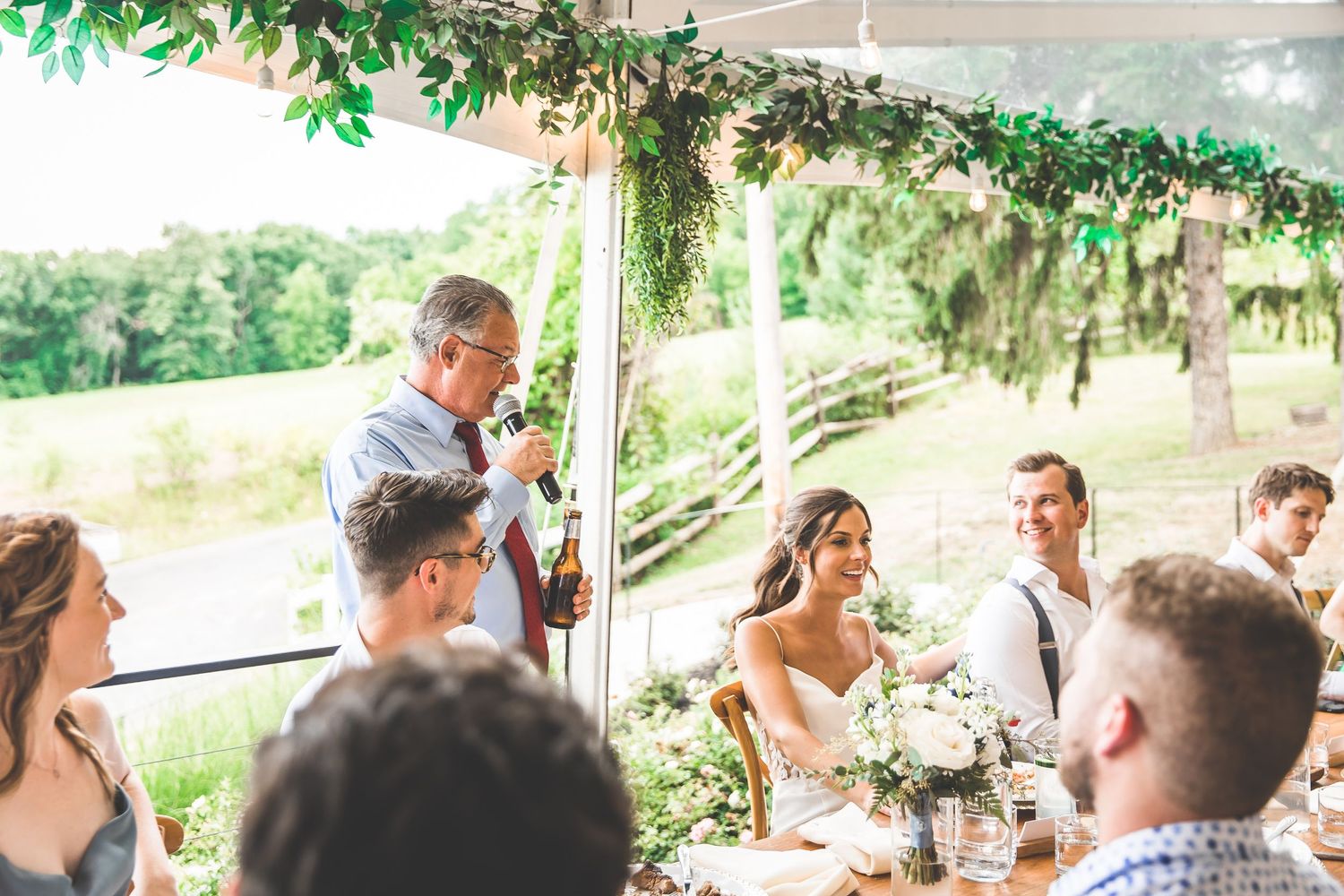 Guests enjoying a wedding reception meal under a tent decorated with hanging greenery.
