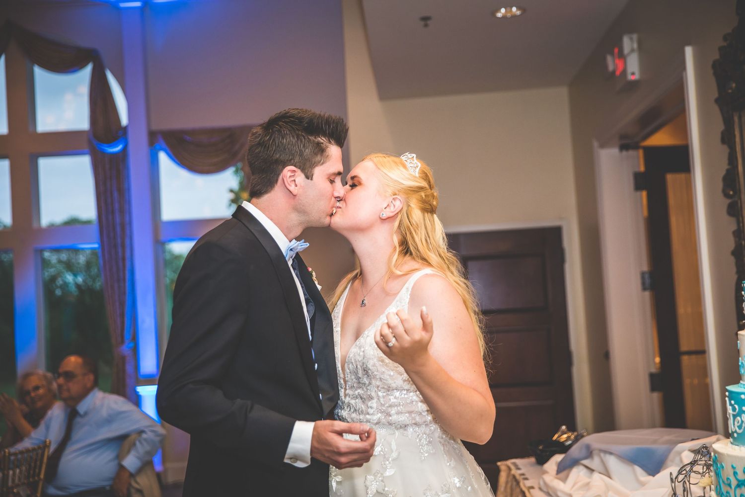 Couple dancing in an elegant reception hall with dramatic blue lighting and chandeliers.