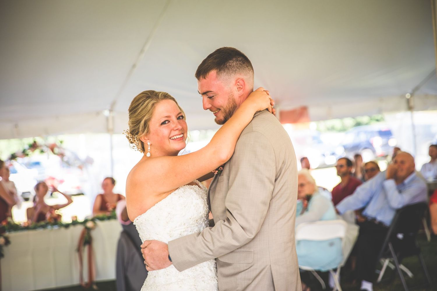 A couple shares their first dance at an outdoor wedding reception under a white tent.