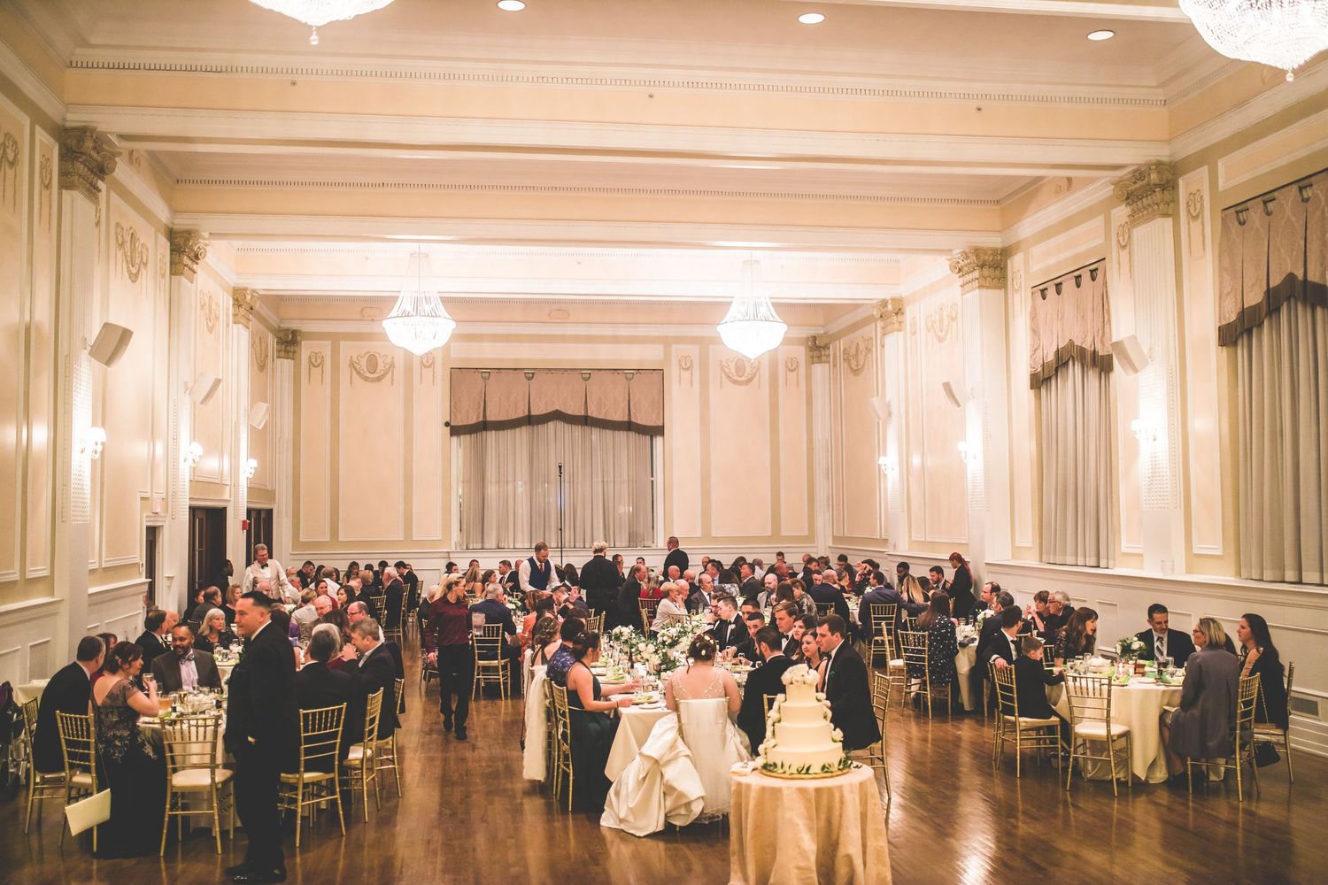 Elegant ballroom filled with guests seated at round tables under crystal chandeliers.