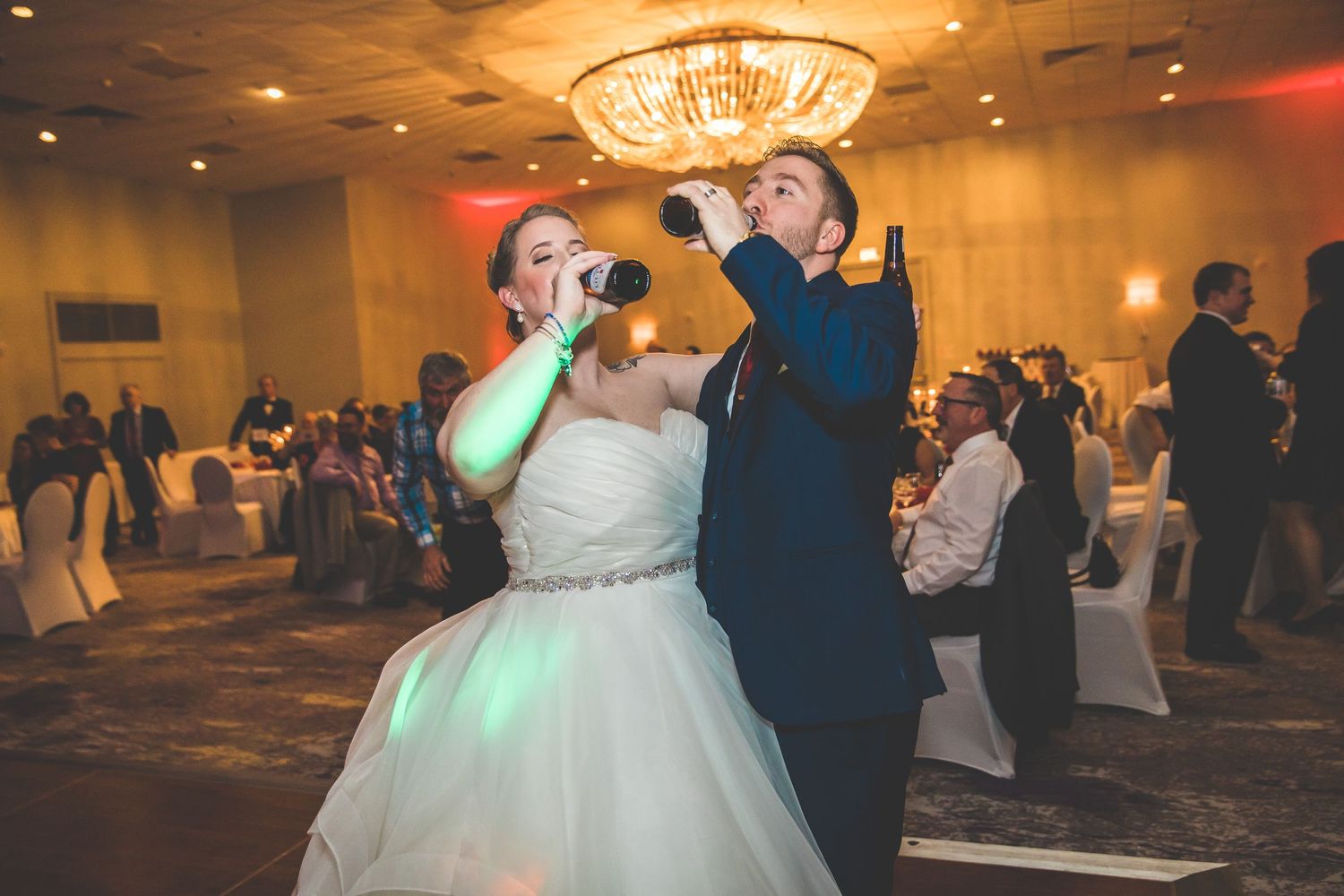 Wedding celebration in an elegant ballroom with chandelier lighting and dancing guests.