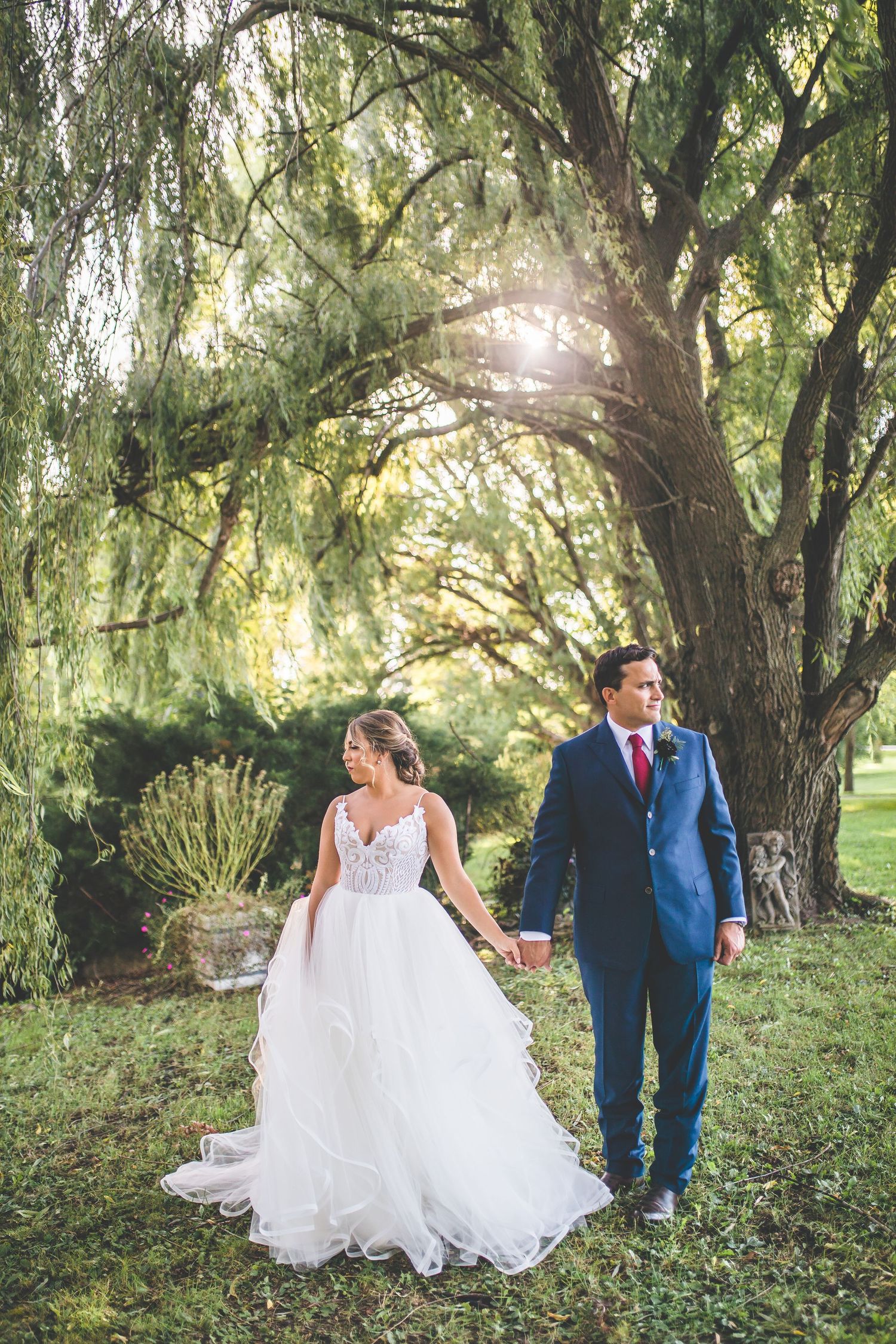 Couple walking through a romantic willow tree garden on their wedding day.