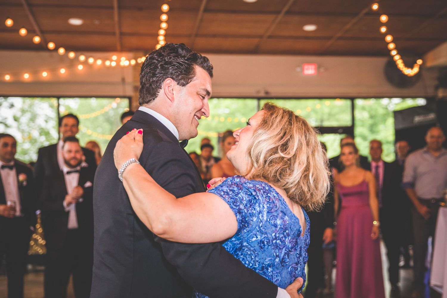 Guests watching as couple shares a dance moment during indoor wedding reception with string lights.