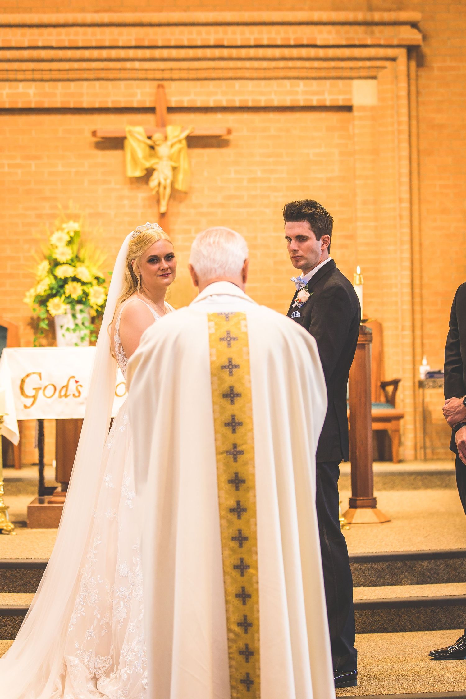 Priest in white robes conducting wedding ceremony at church altar.