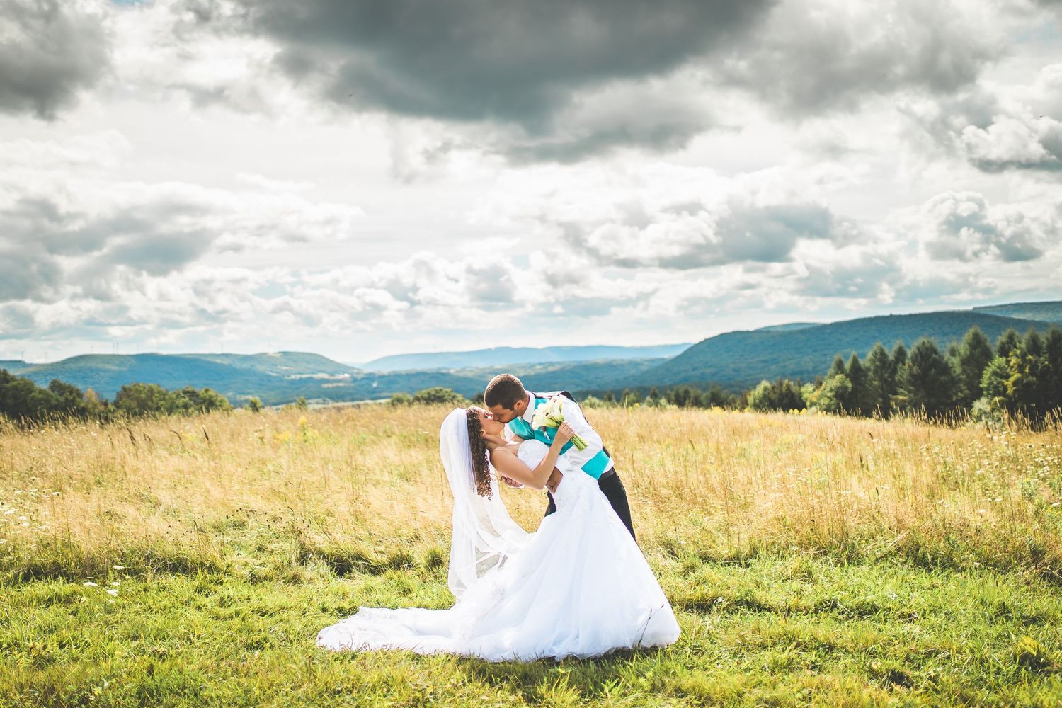 Dramatic wedding photos against cloudy sky in mountain meadow.