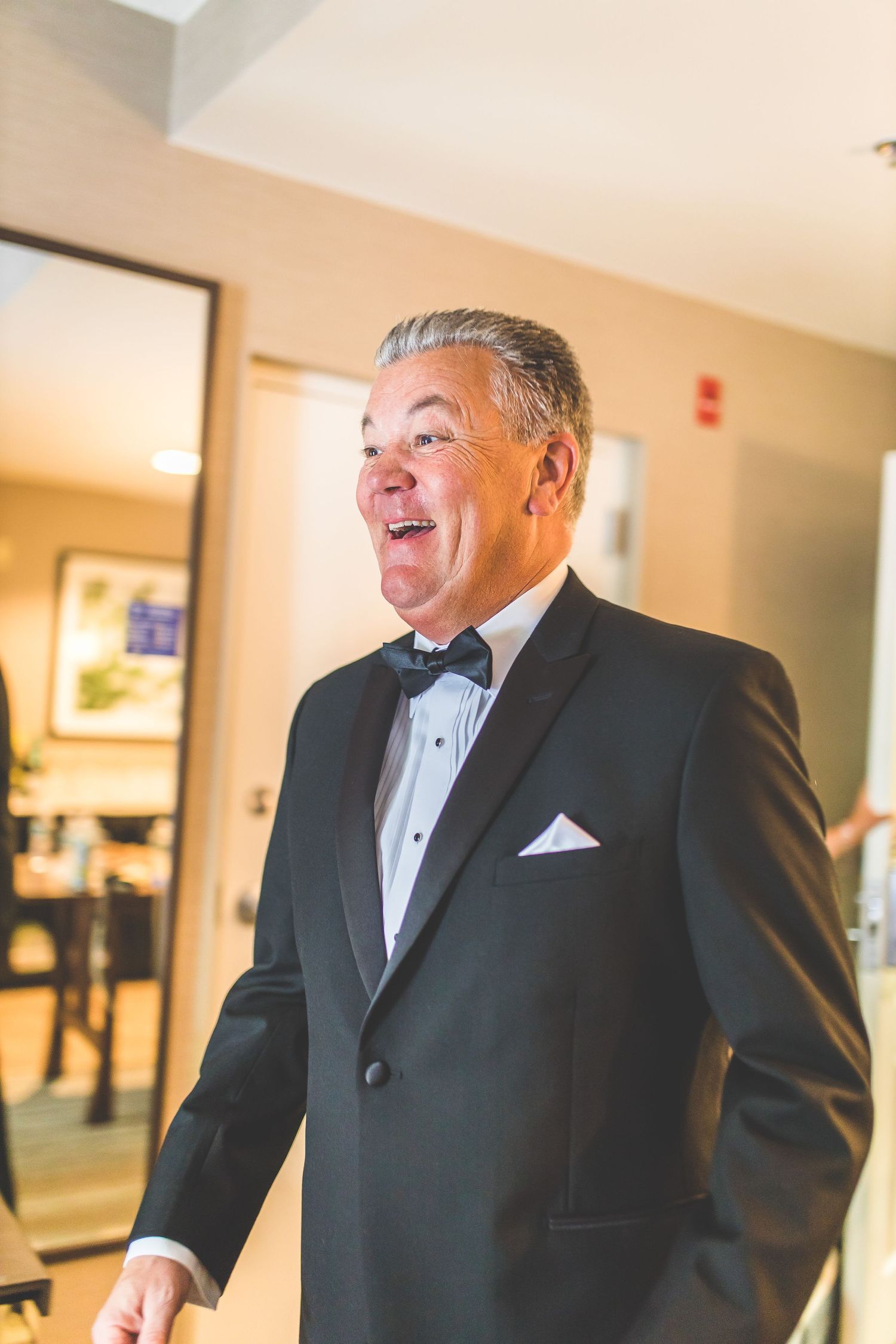 A person wearing a classic black tuxedo with bow tie smiles warmly during a formal event.
