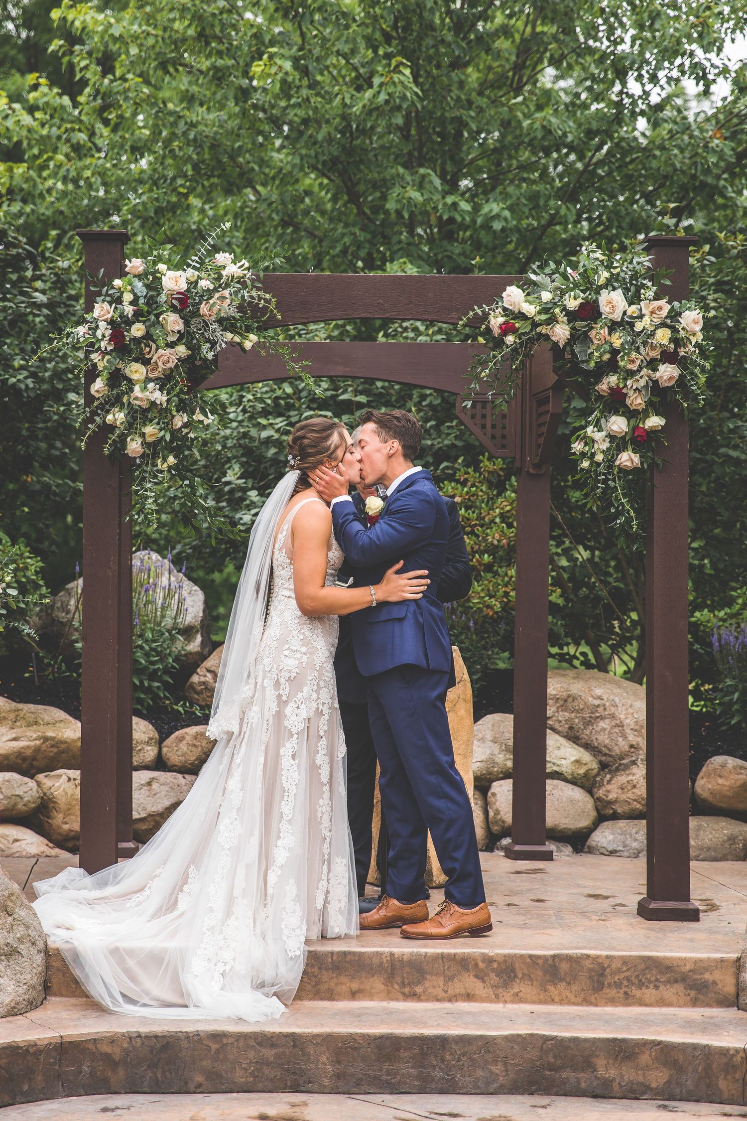 Wedding couple sharing romantic moment under wooden pergola decorated with blush roses.