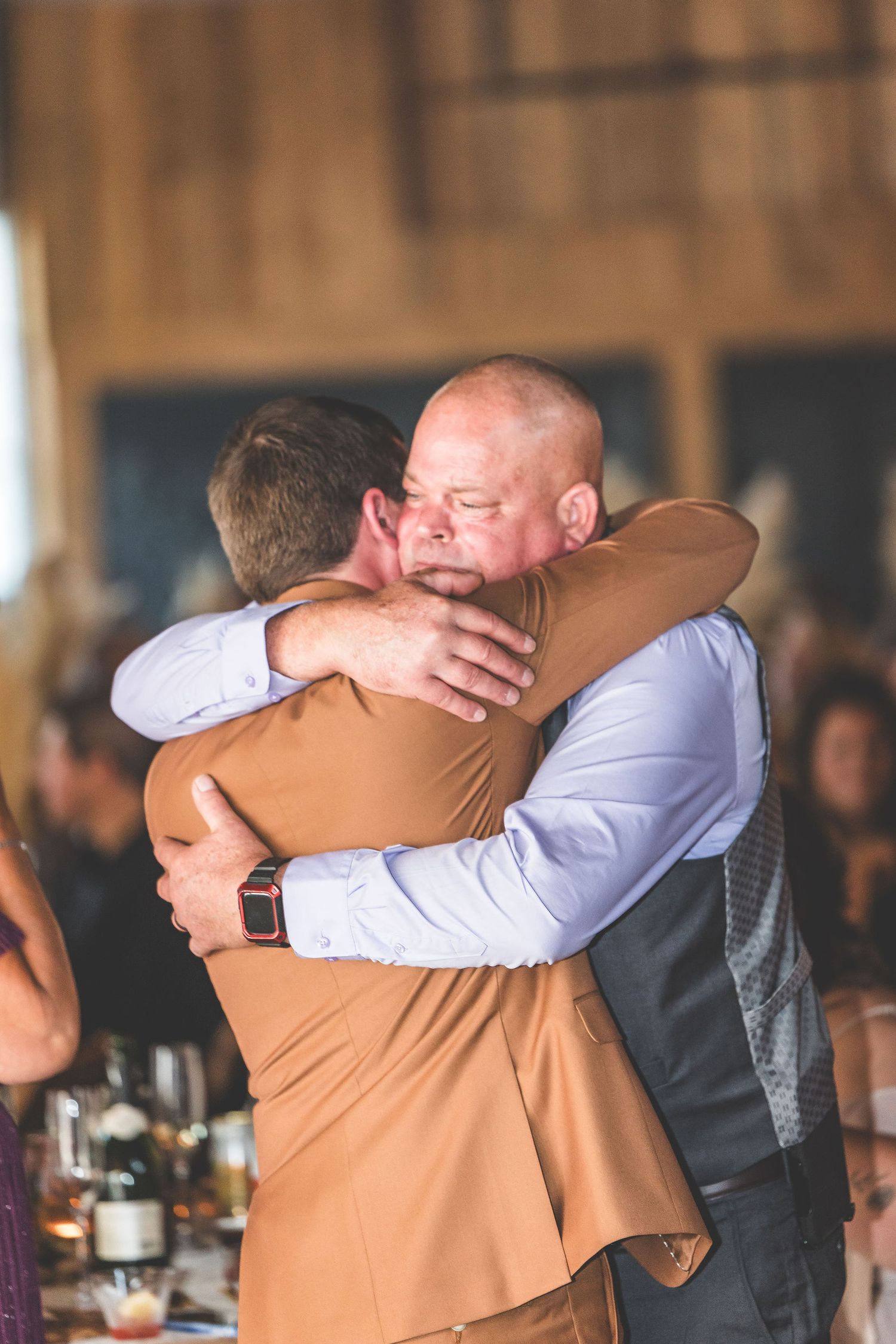 Emotional groomsmen share heartfelt embraces during wedding reception celebrations.