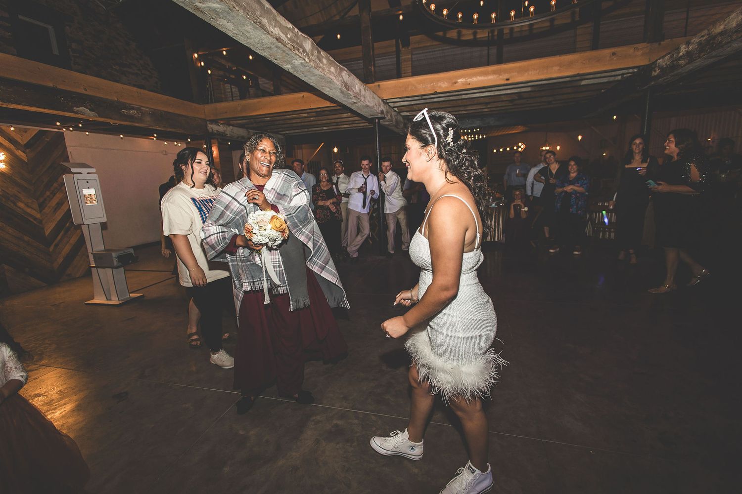 Wedding celebration with dancers in casual attire on rustic indoor dance floor.