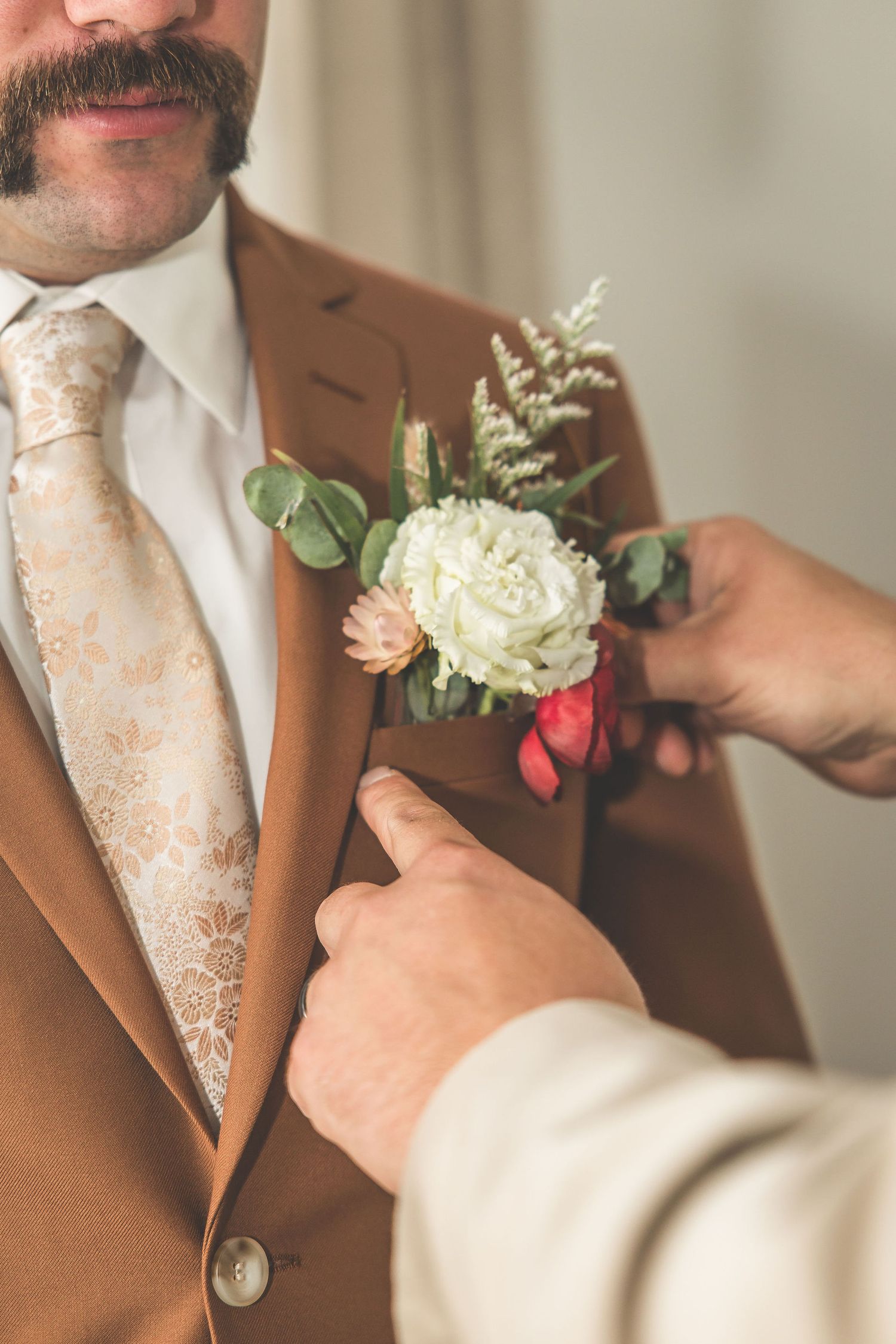 A white and peach boutonniere is pinned to a brown suit jacket.