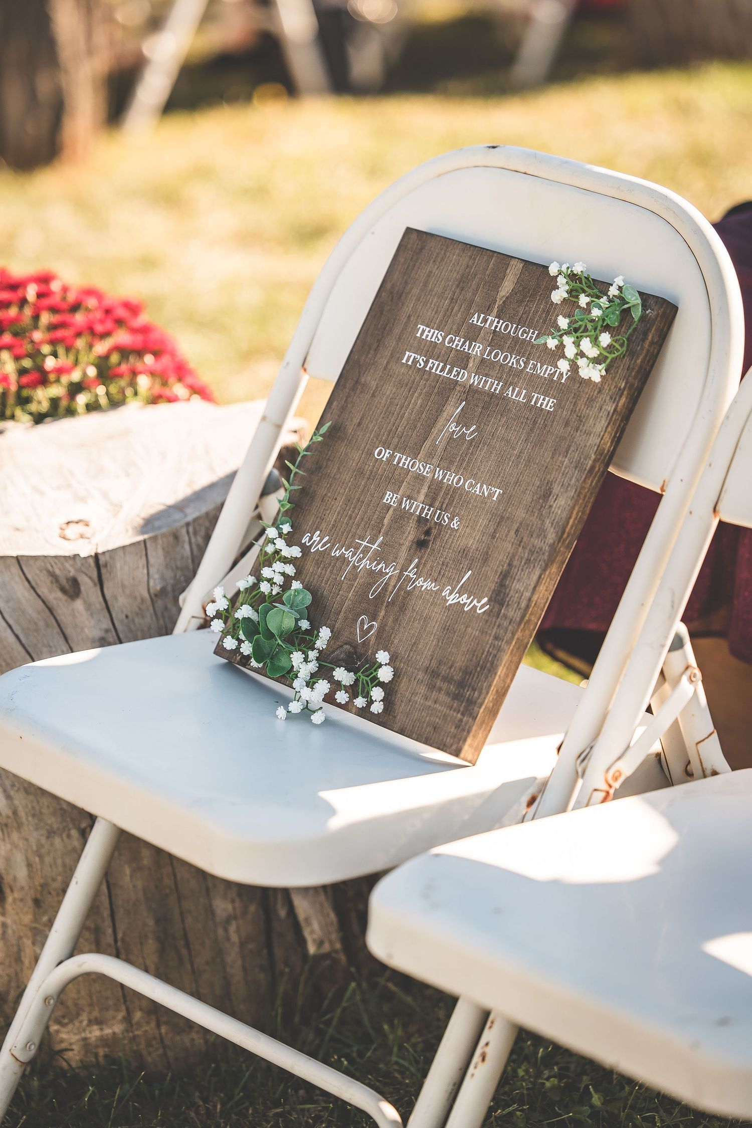 Wooden wedding program signs displayed on white folding chairs in sunlight.