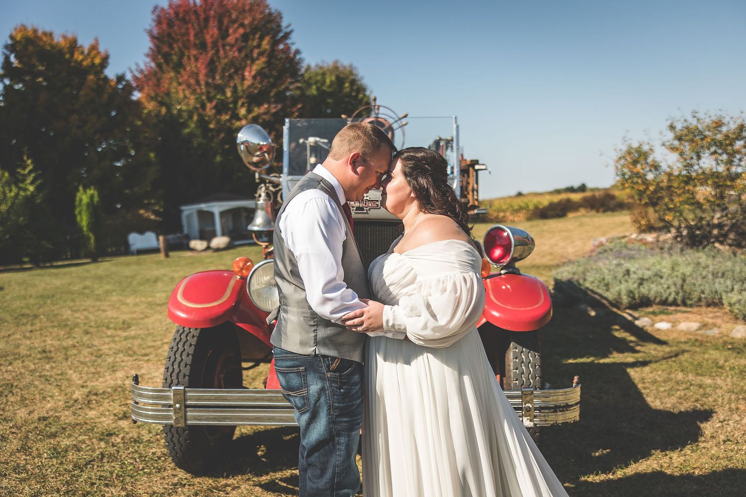 Couple poses with antique fire truck during autumn wedding photoshoot.