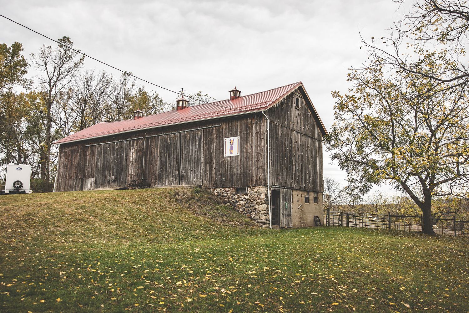 Panoramic view of rustic barns on a hillside with fall foliage.