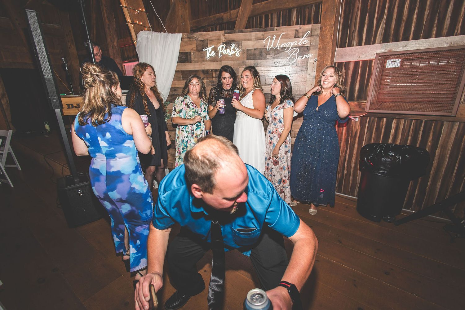 People dancing and enjoying themselves at a dimly lit barn wedding reception.