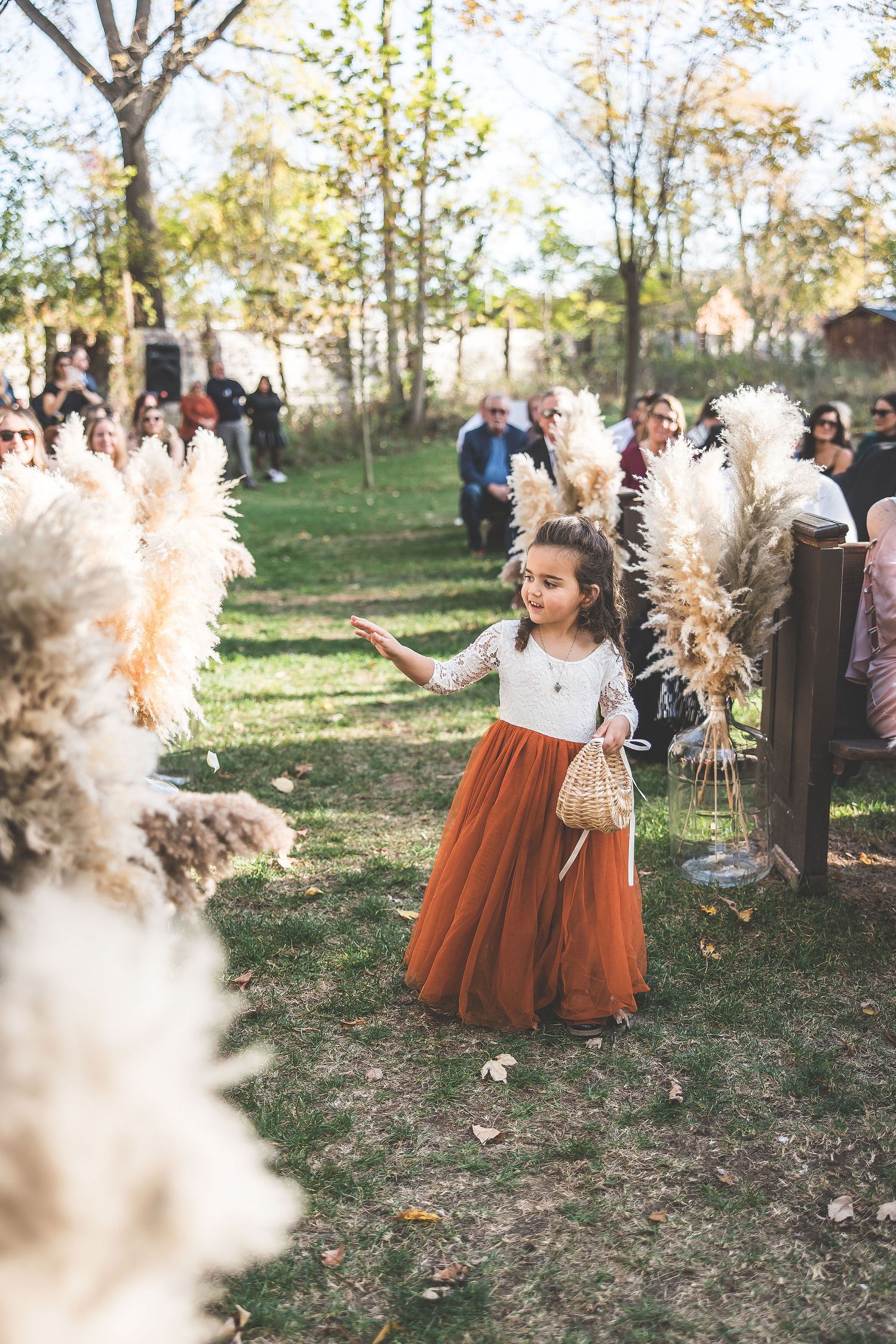 Decorative pampas grass lines an outdoor autumn wedding ceremony with rust-colored accents.