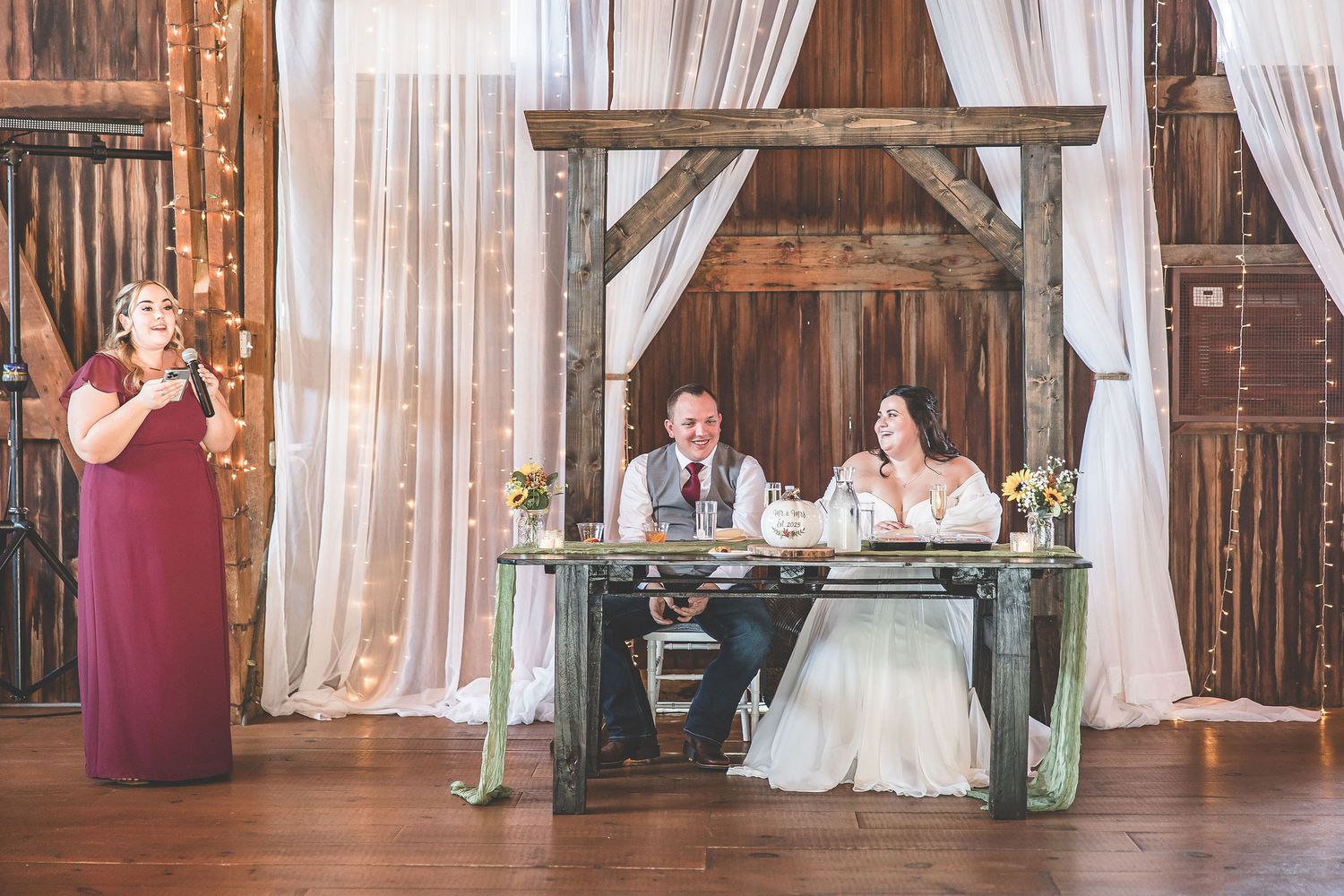 A rustic barn wedding reception space with elegant white draping and wooden beams.