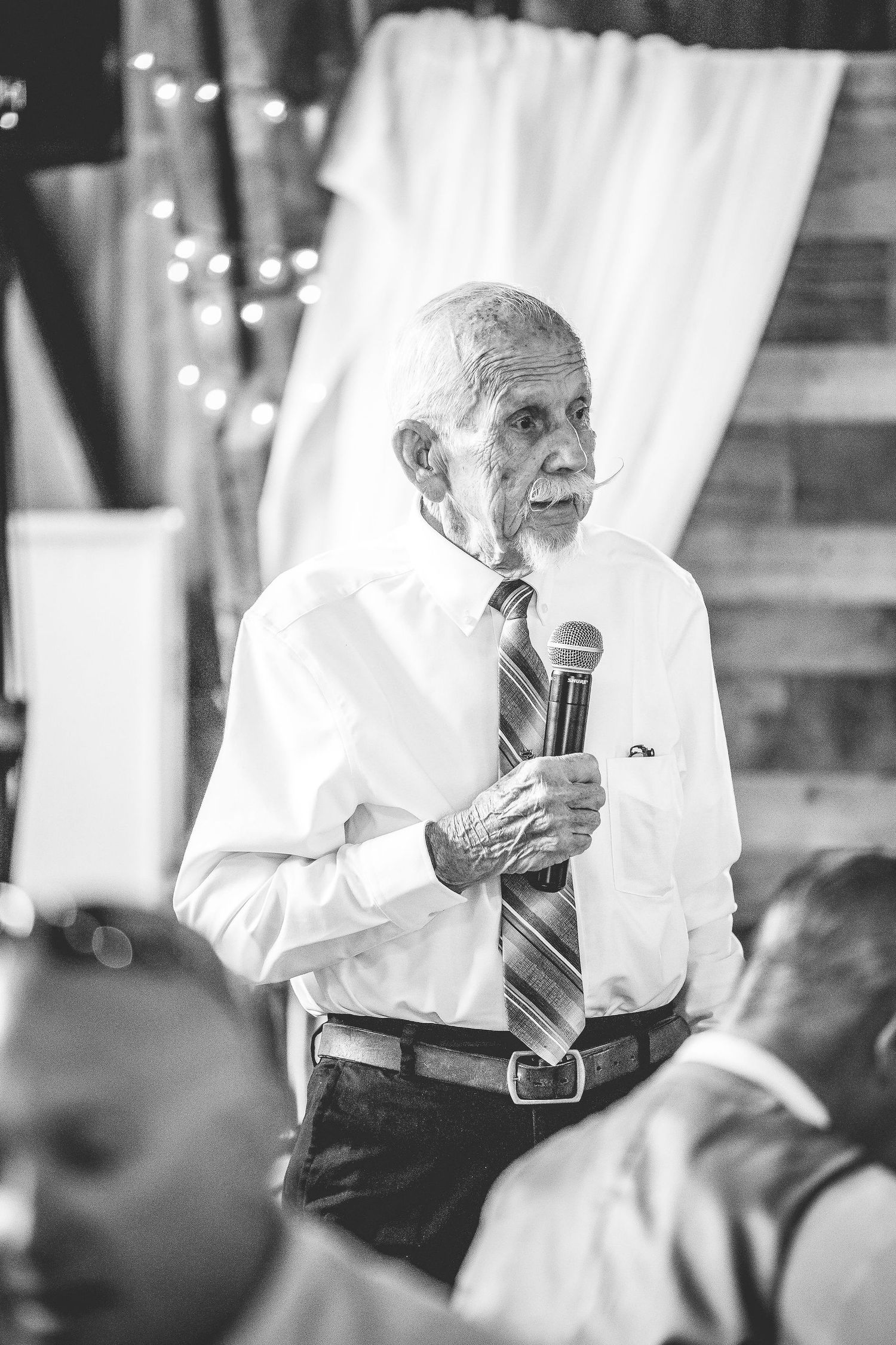 A speaker holds a microphone during a wedding reception in a rustic barn setting.