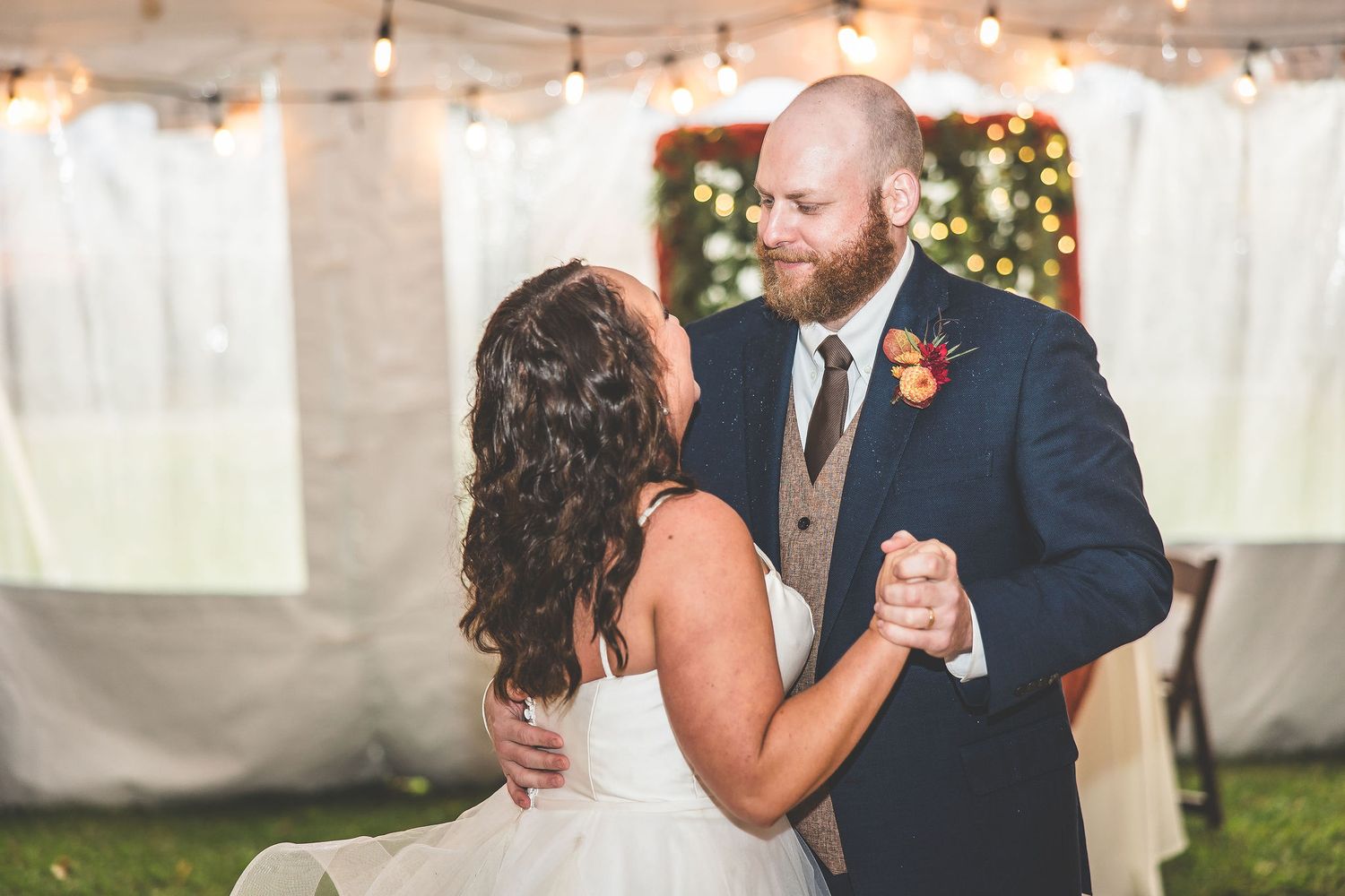 Couple sharing first dance under string lights in elegant tented wedding reception.