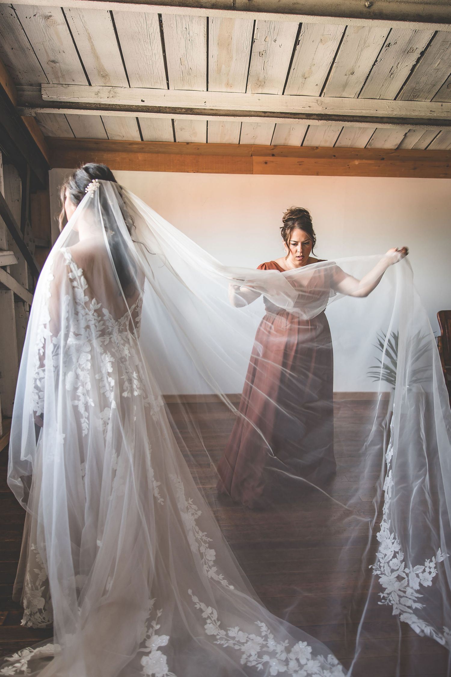 Artistic wedding photo with flowing veil creating dramatic movement in rustic attic space.
